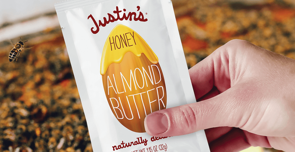 Hand holding Honey Almond Butter squeezepack. Bee panel visible in the background.