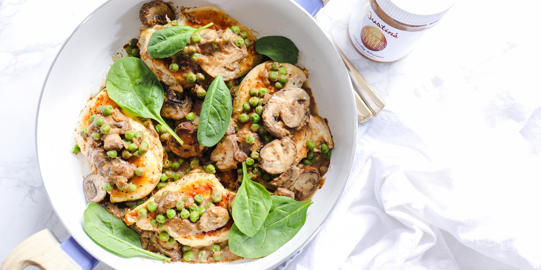 Chicken with Savory Almond Butter Sauce in a white pan with wooden handles in a white background with a white cloth