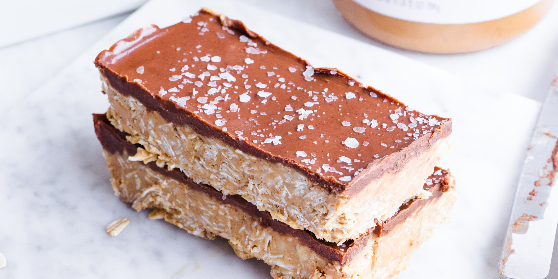 Easy No Bake Peanut Butter Granola Bars out of the tray with Justin's peanut butter jar on a white background side view