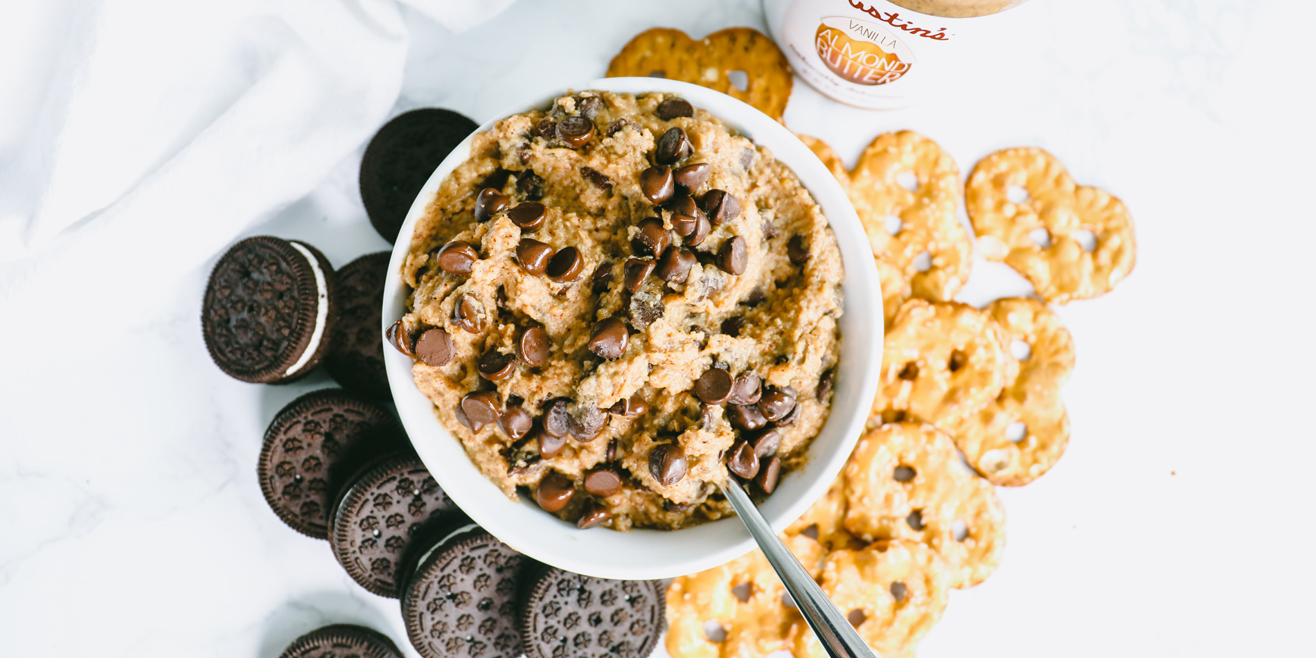 Gluten-Free Chocolate Chip Cookie Dough Dip in a bowl with cream chocolate cookies and salted pretzels scattered underneath