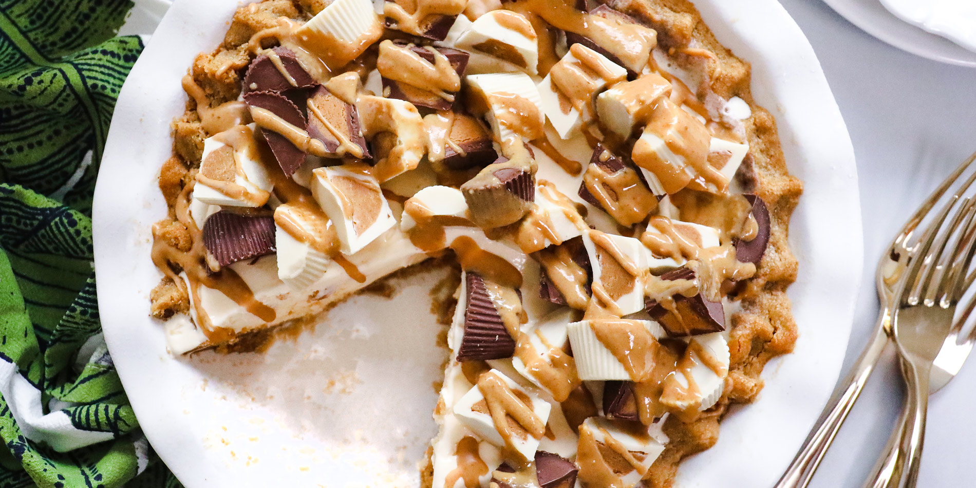 Gluten Free Peanut Butter Cookie Pie with a missing slice on white plate with green cloth in the white background with forks