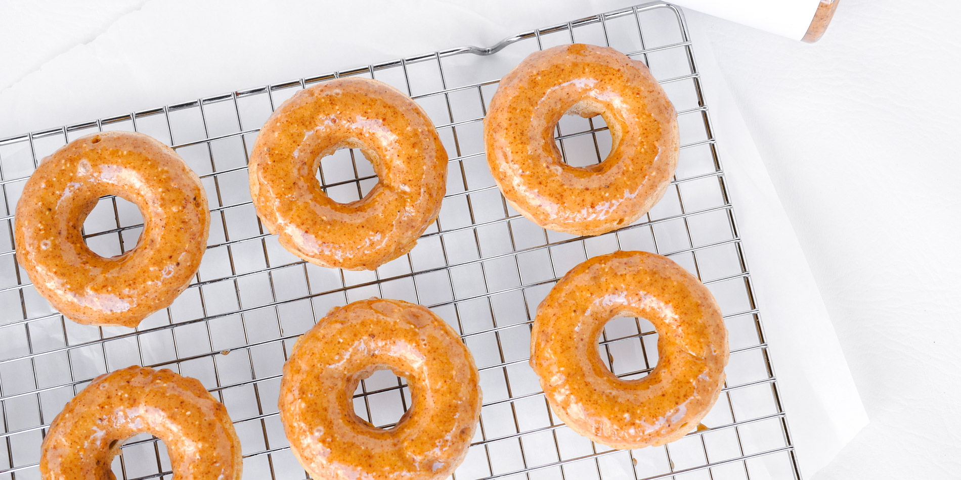 Guilt Free Maple Almond Butter Doughnuts on a cooling tray in a white background with a peanut butter jar