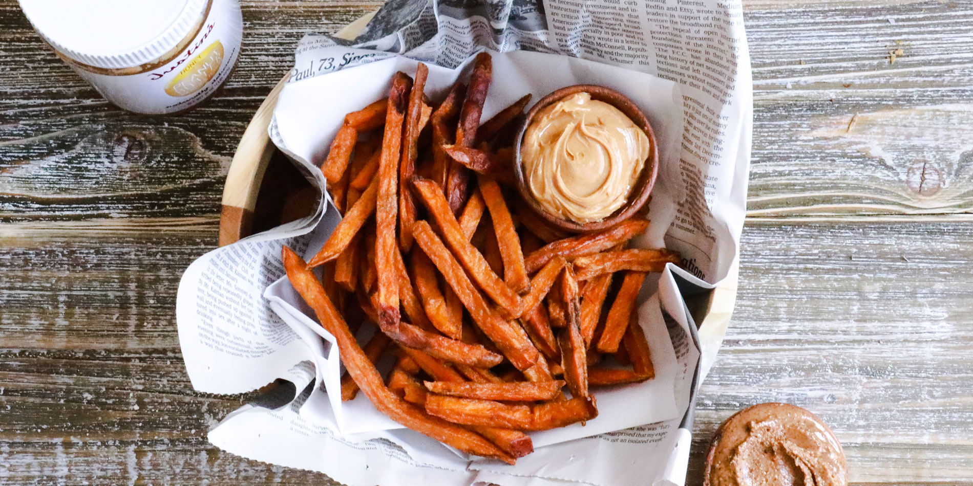 Honey Sweet Potato Fries in parchment paper with Justin's honey peanut butter dip in a wooden bowl and background