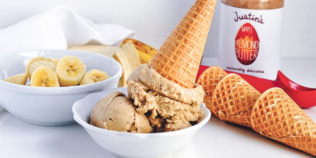 Maple Almond Butter Banana Nice Cream on a cone dunked in a small white bowl with slices bananas in another bigger white bowl