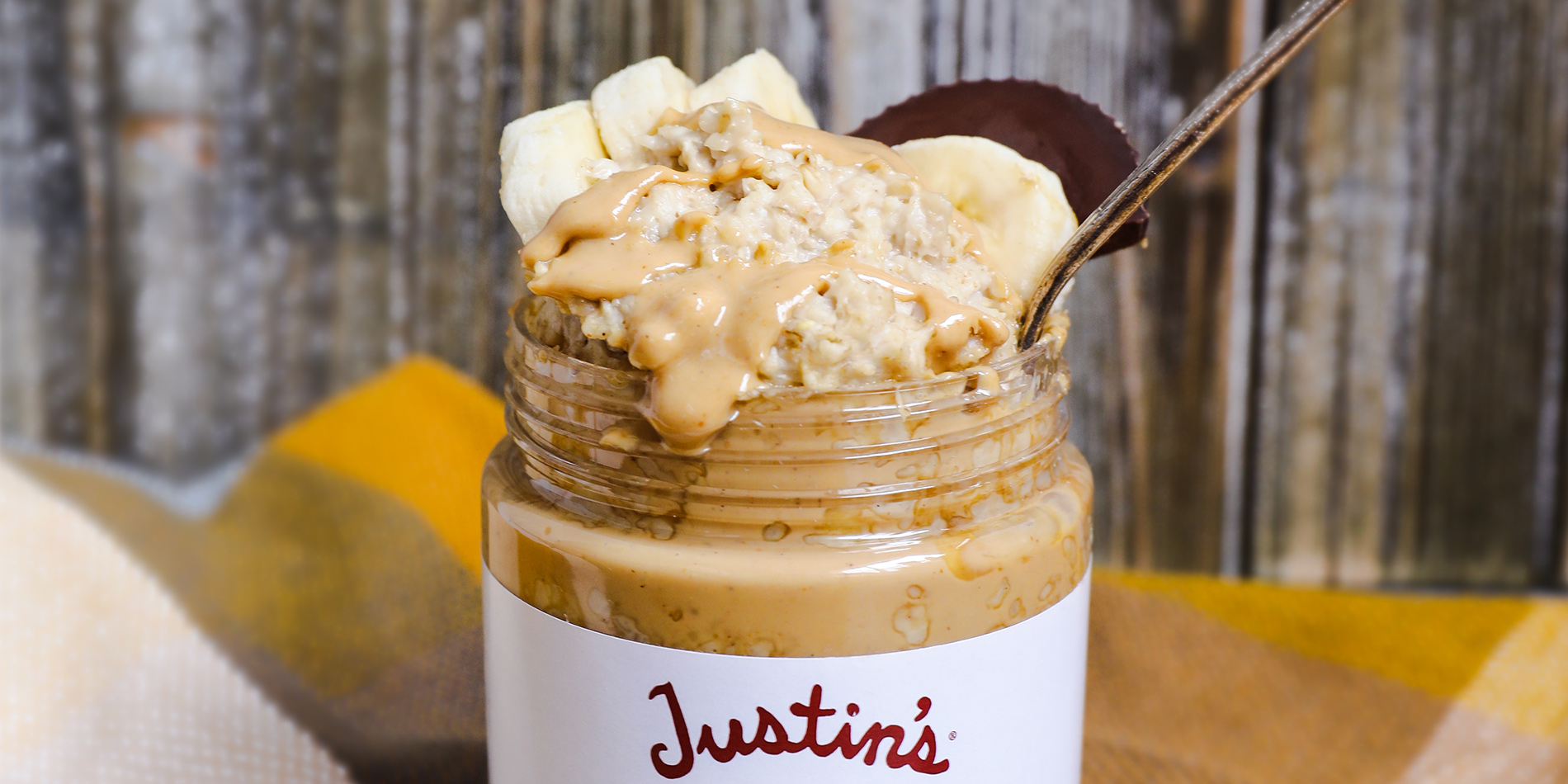 Nutty Overnight Oats in a Justin's Classic Cashew Peanut Butter jar on a blue and brown gingham cloth with a wooden backdrop