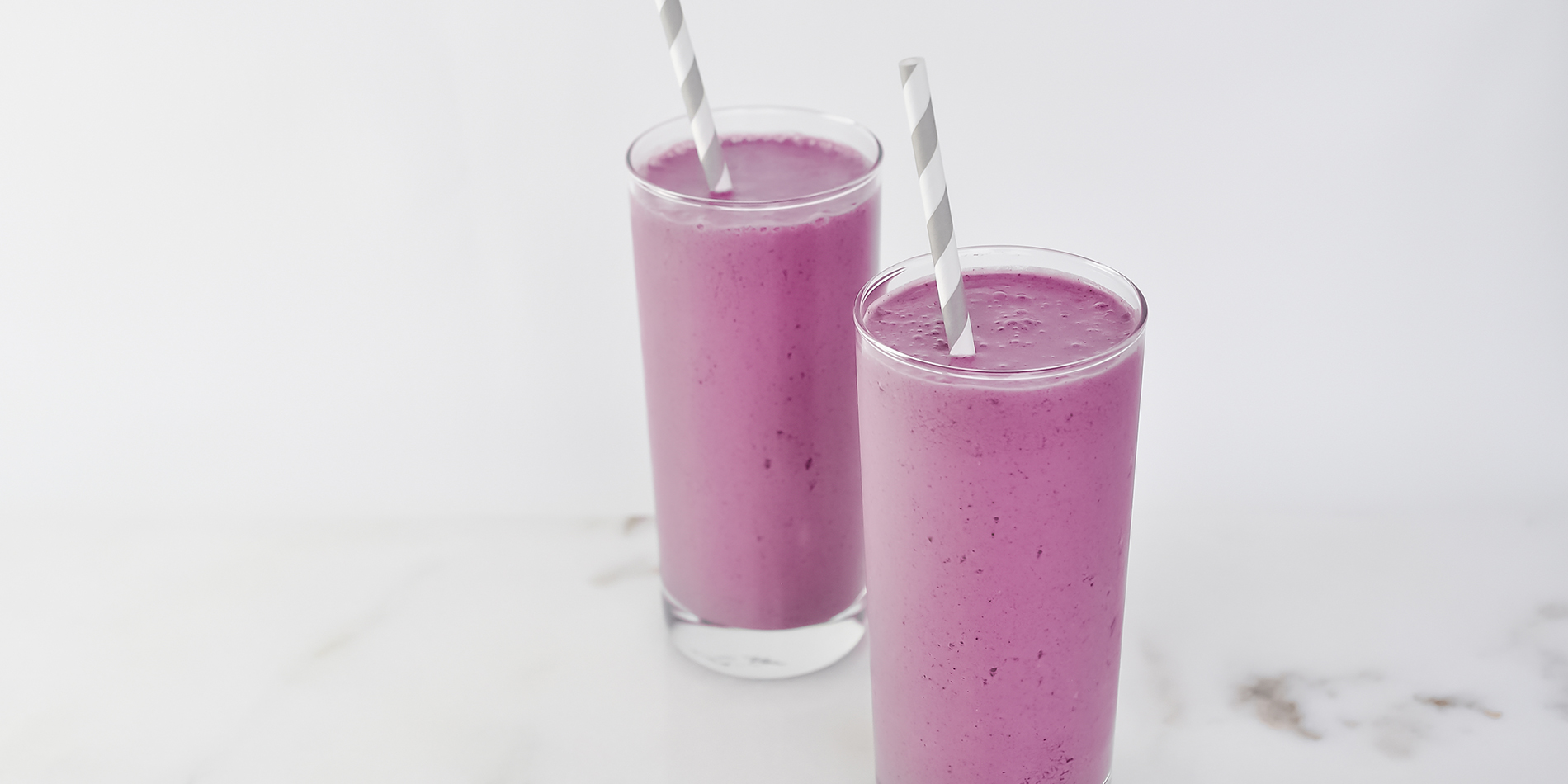 Peanut Butter and Jelly Smoothie in clear cups with white and gray striped straws on a white background