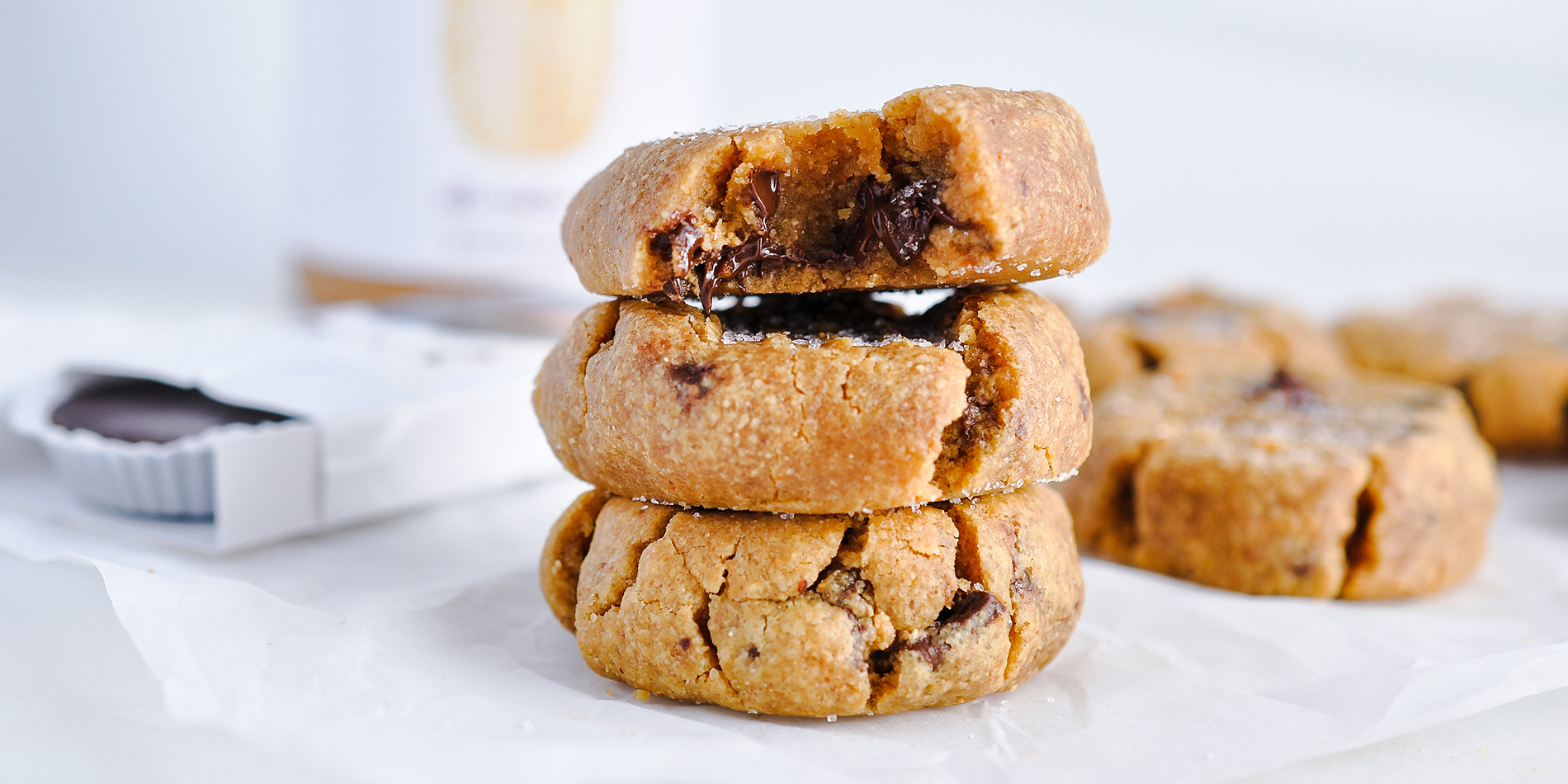 Peanut Butter Cookies stacked with the top one bit revealing the melted chocolate on a white parchment on white background