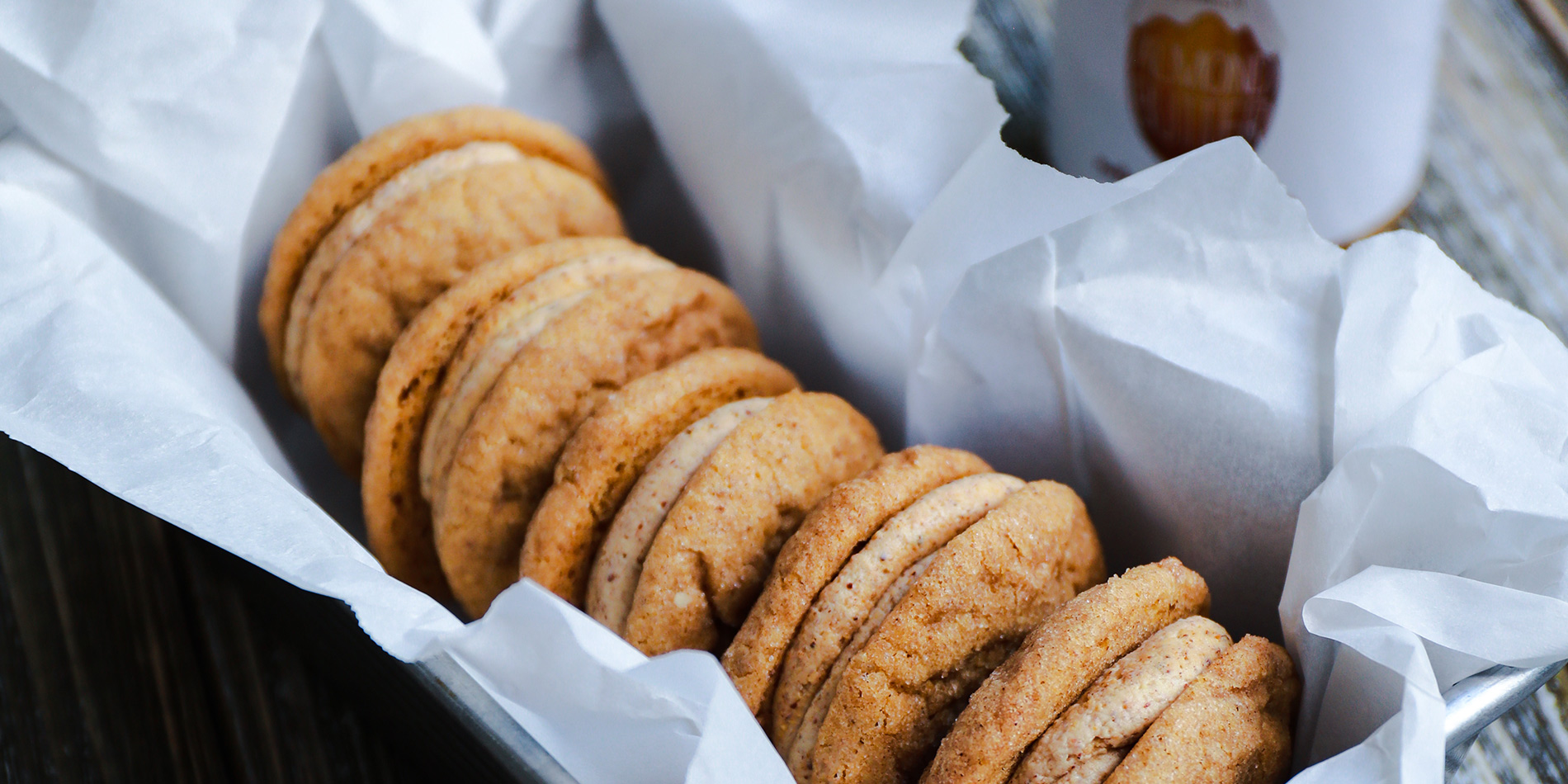 Pumpkin Vanilla Almond Snickerdoodlewiches in a tray and one bitten and put on a white plate on a wooden background