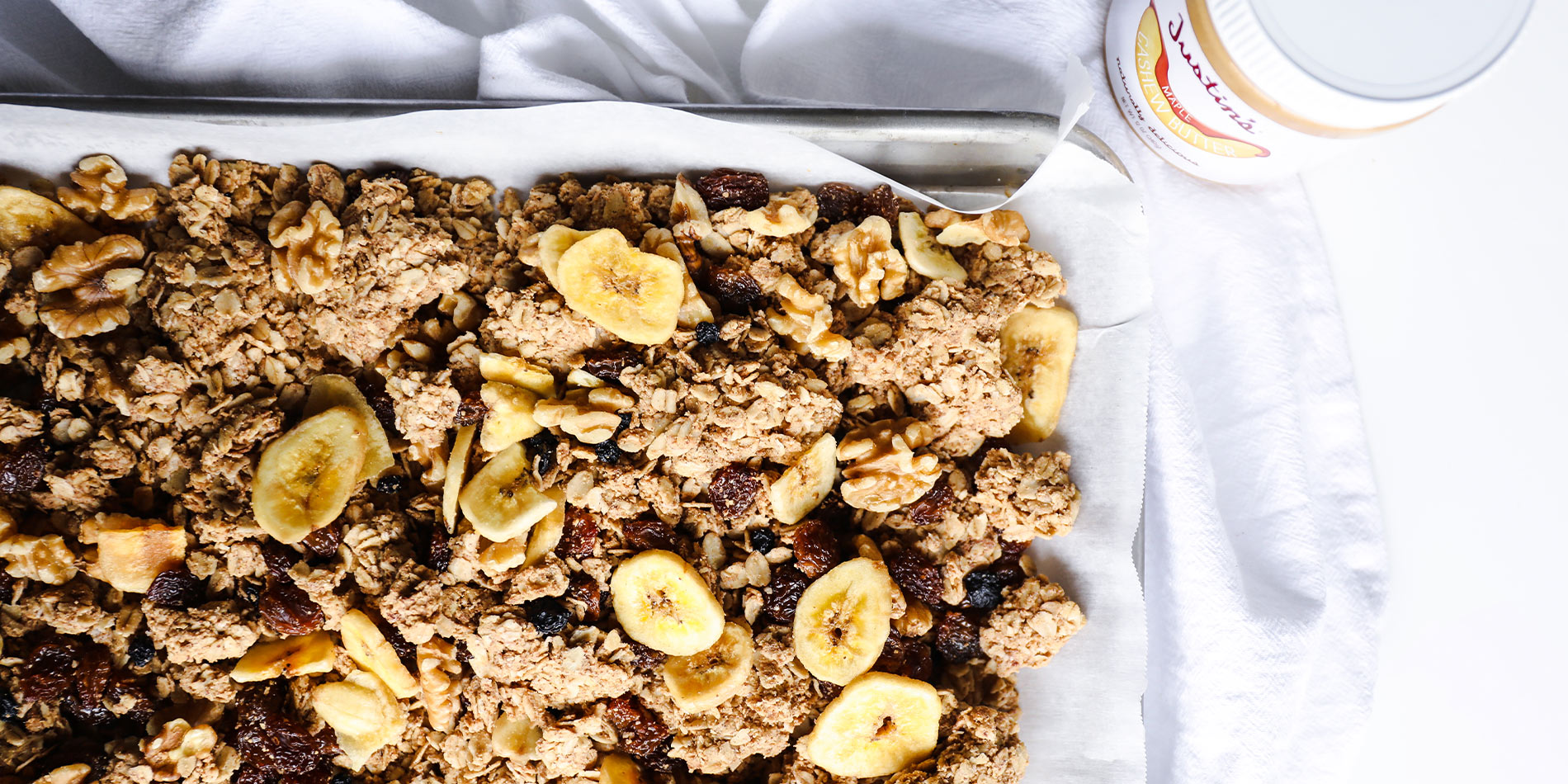 The Best Nut Butter Granola on white parchment sheet in a gray tray which is on a white cloth on a white background