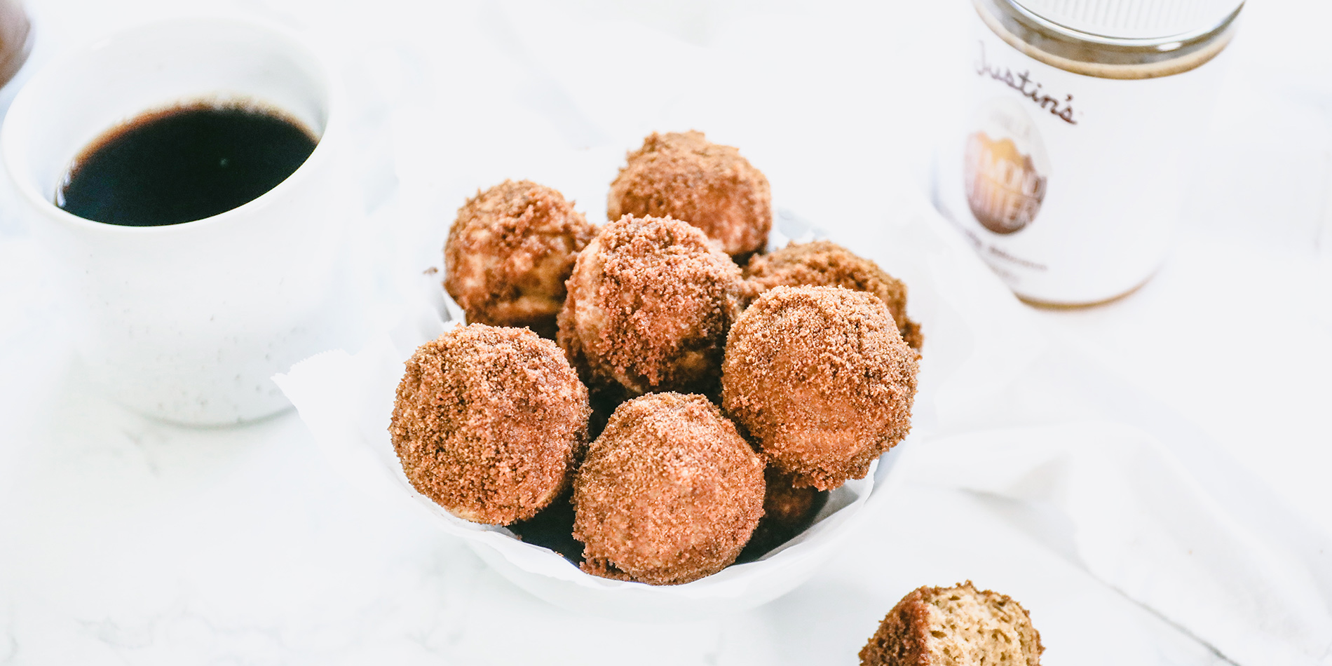 Vanilla Almond Baked Doughnut Holes in a white bowl with coffee and Justin's peanut butter jar