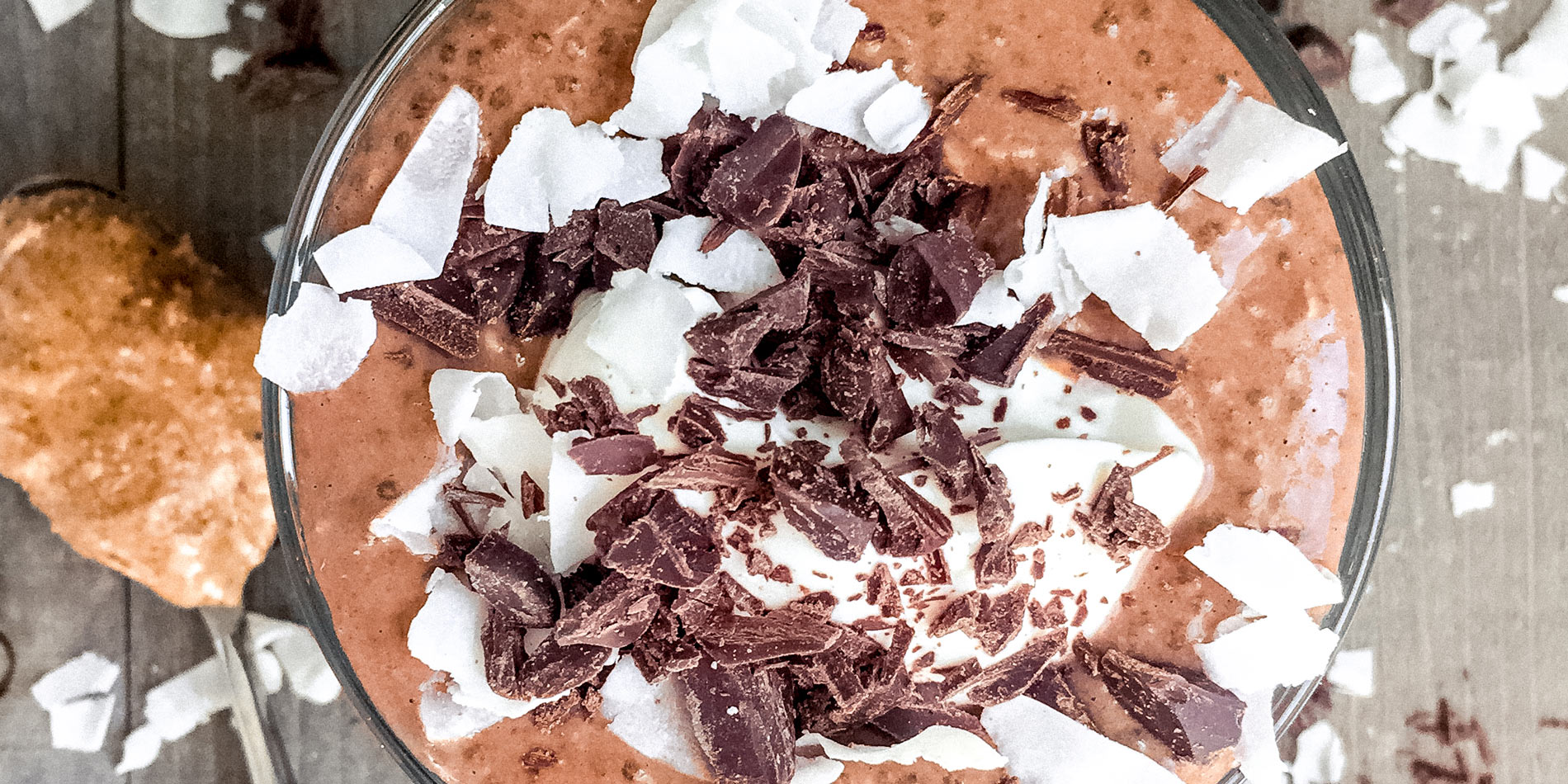 Coconut Almond Chia Pudding with chocolate and coconut flakes and a spoon in a wood background (bird's eye view)