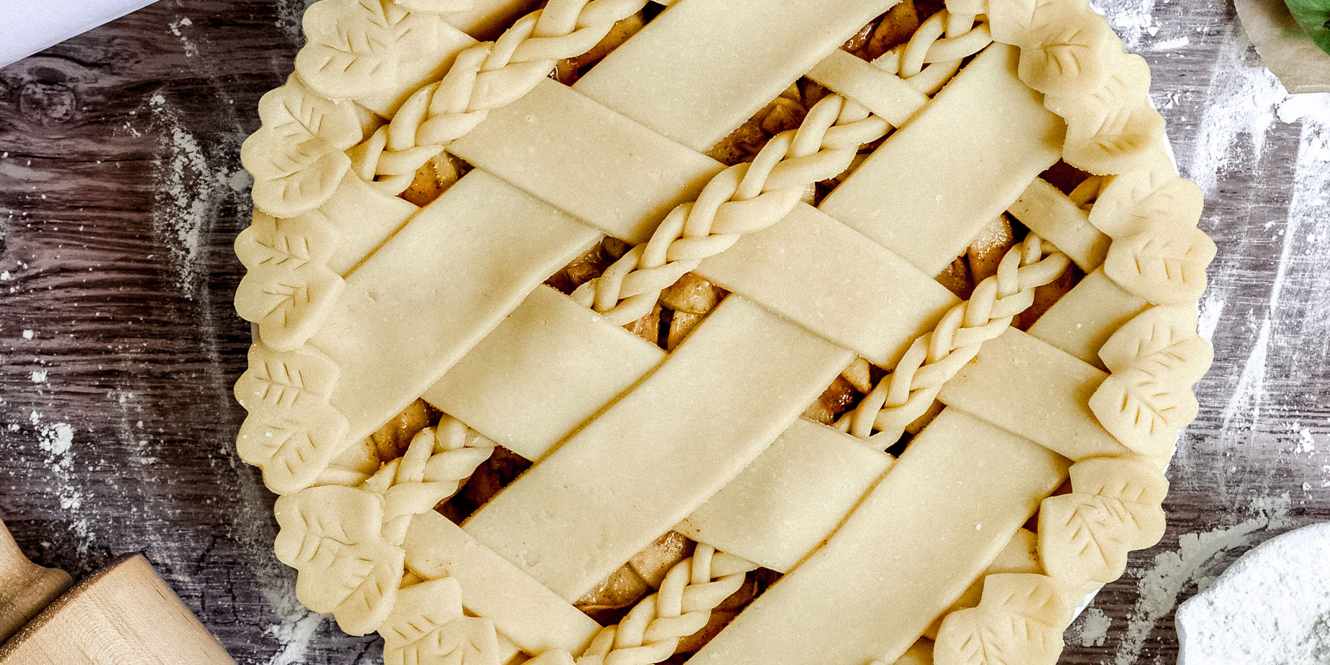 Maple Almond Butter Apple Pie with green apples, flour, peanut butter and baking tools scattered on a brown wooden background