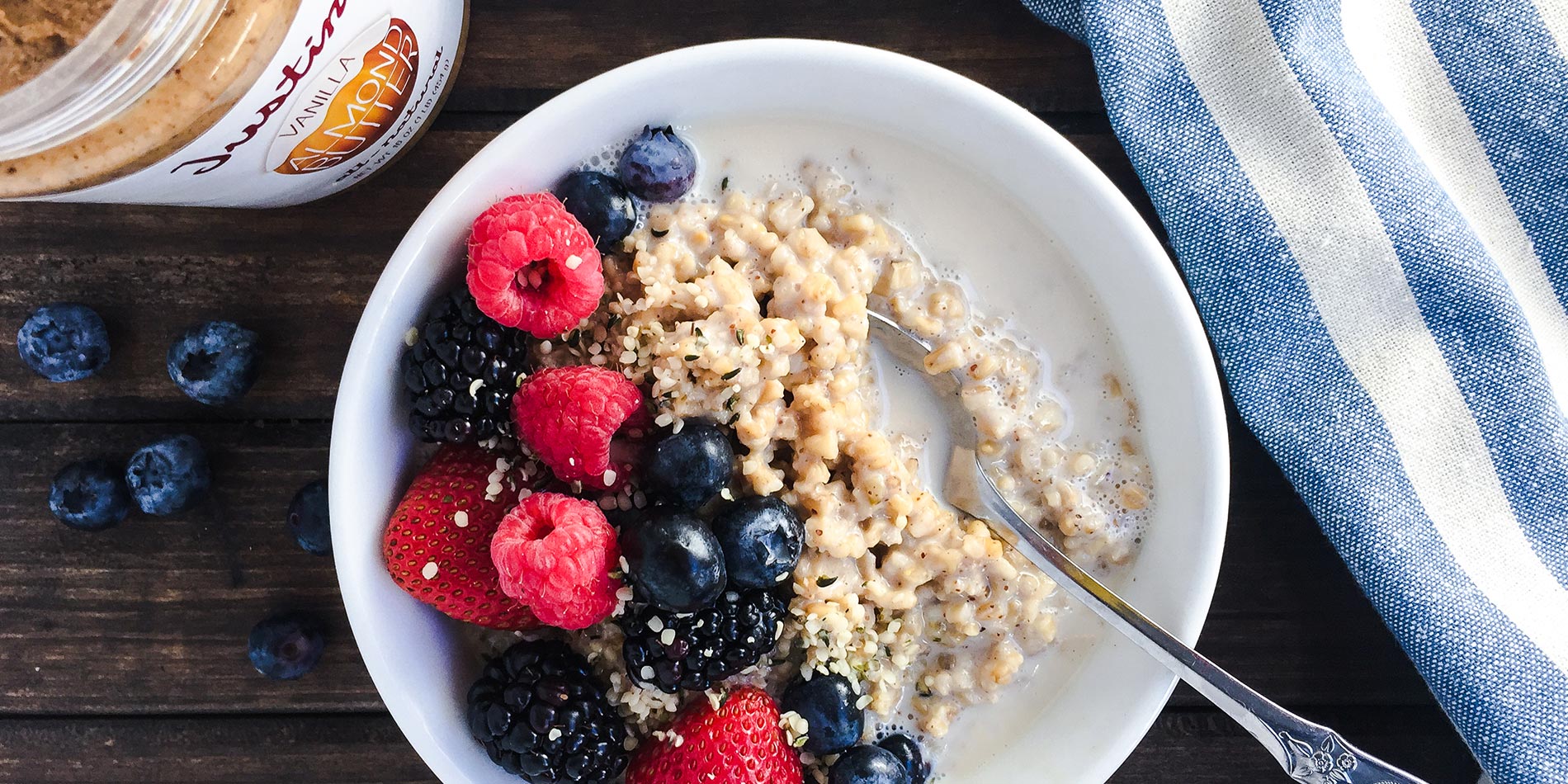 Vanilla Sweet Cream Berry Oatmeal in a white bowl on a dark wood background with a striped blue cloth