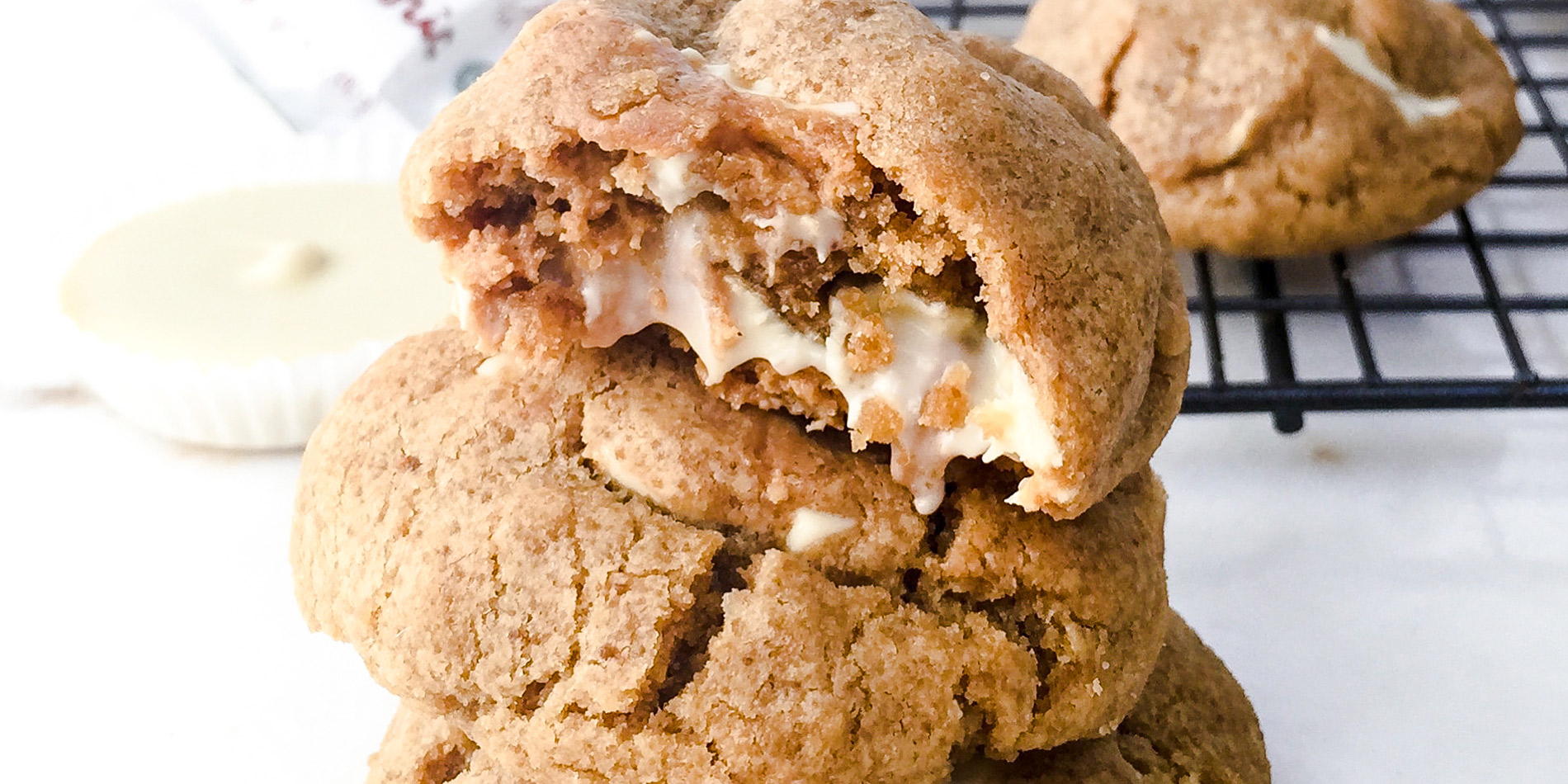 White Chocolate Peanut Butter Cup Cookies stacked and the top one bitten on a white background with a black cooling tray