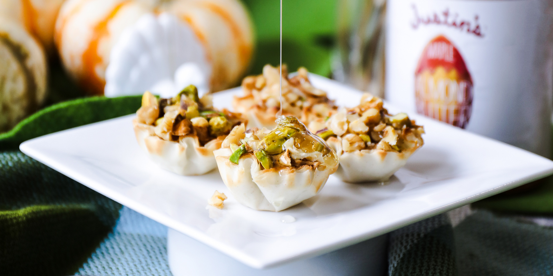 Almond Butter Baklava Bites with honey dripping from top and placed on a white plate and fall decorations in the background