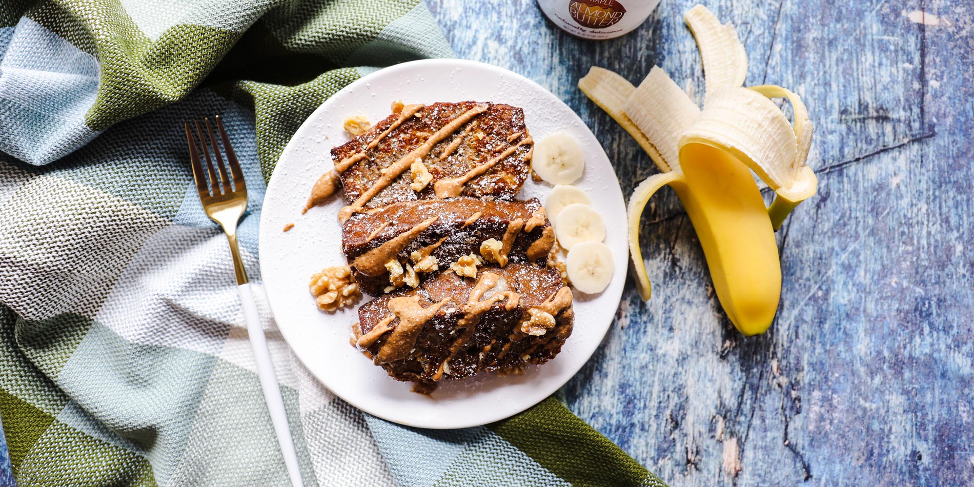 Almond Butter Banana Bread French Toast on a white plate on top of a blue-green table cloth placed on a blue wood background