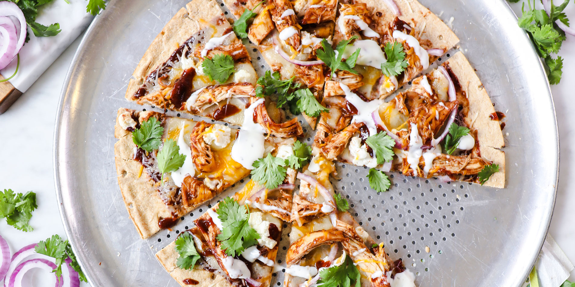 Almond Butter BBQ Chicken Pizza on a round metal pan with one piece on a separate white plate on a white marble background