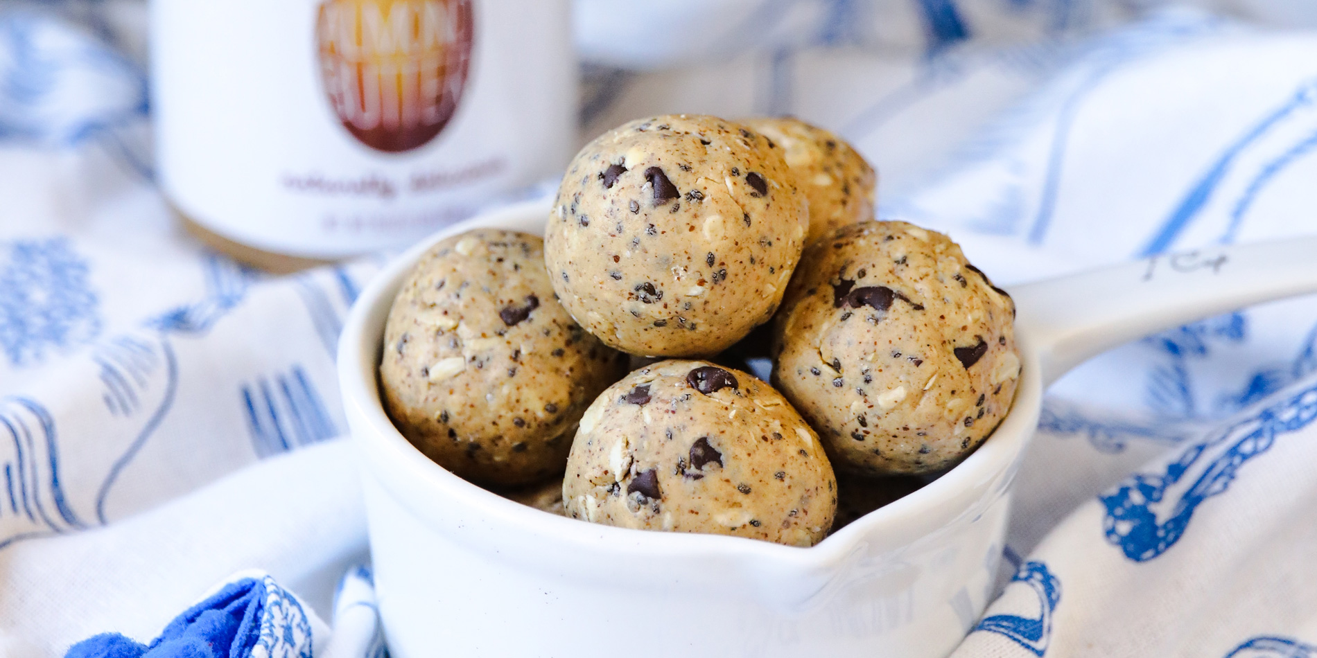 Cookie Dough Protein Balls in a white measuring cup on top of a blue patterned white cloth on top of a wood background