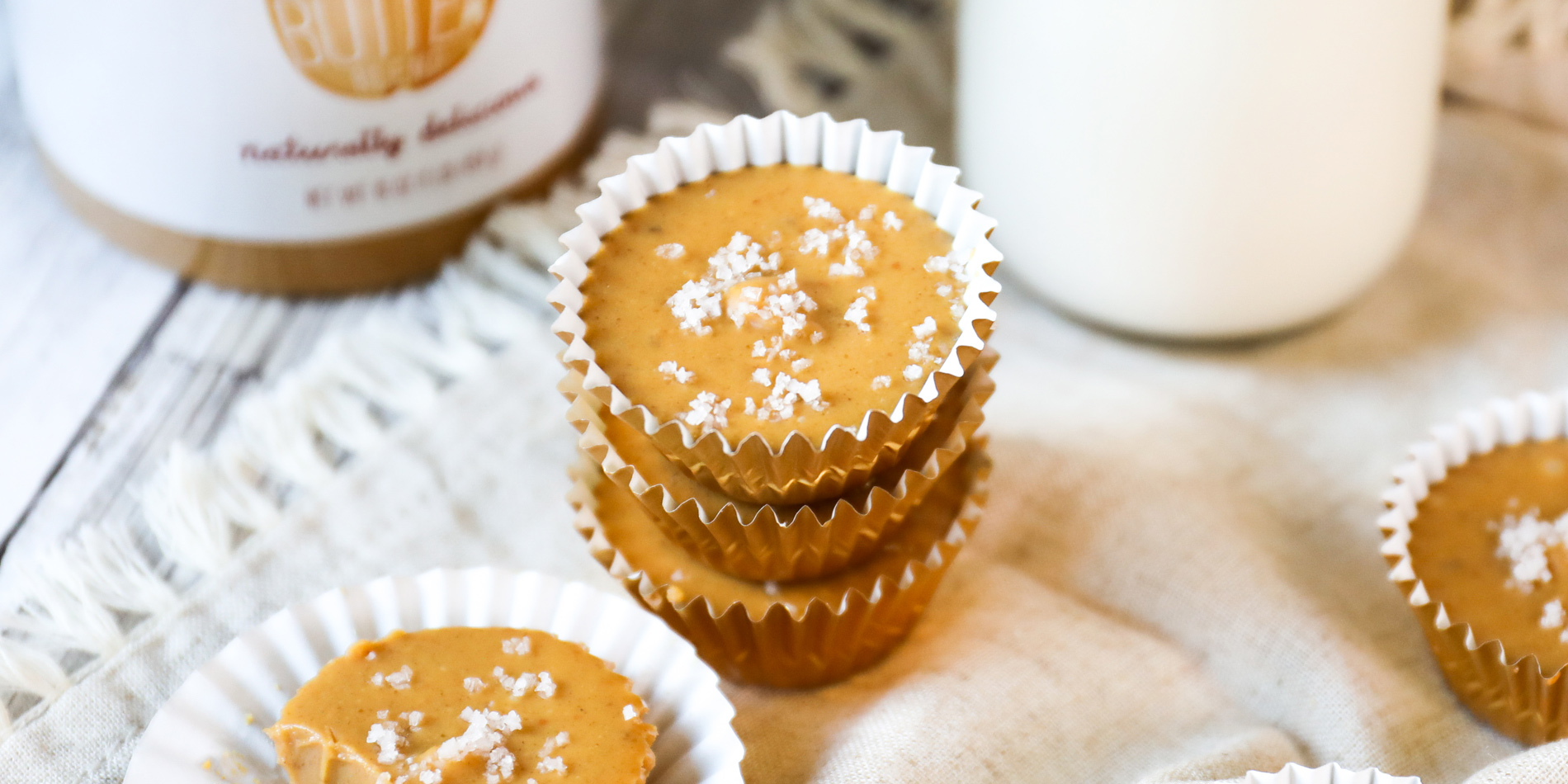 Easy Peanut Butter Fudge in cupcake wrappers stacked on a cloth with Justin's peanut butter and milk jar in the background