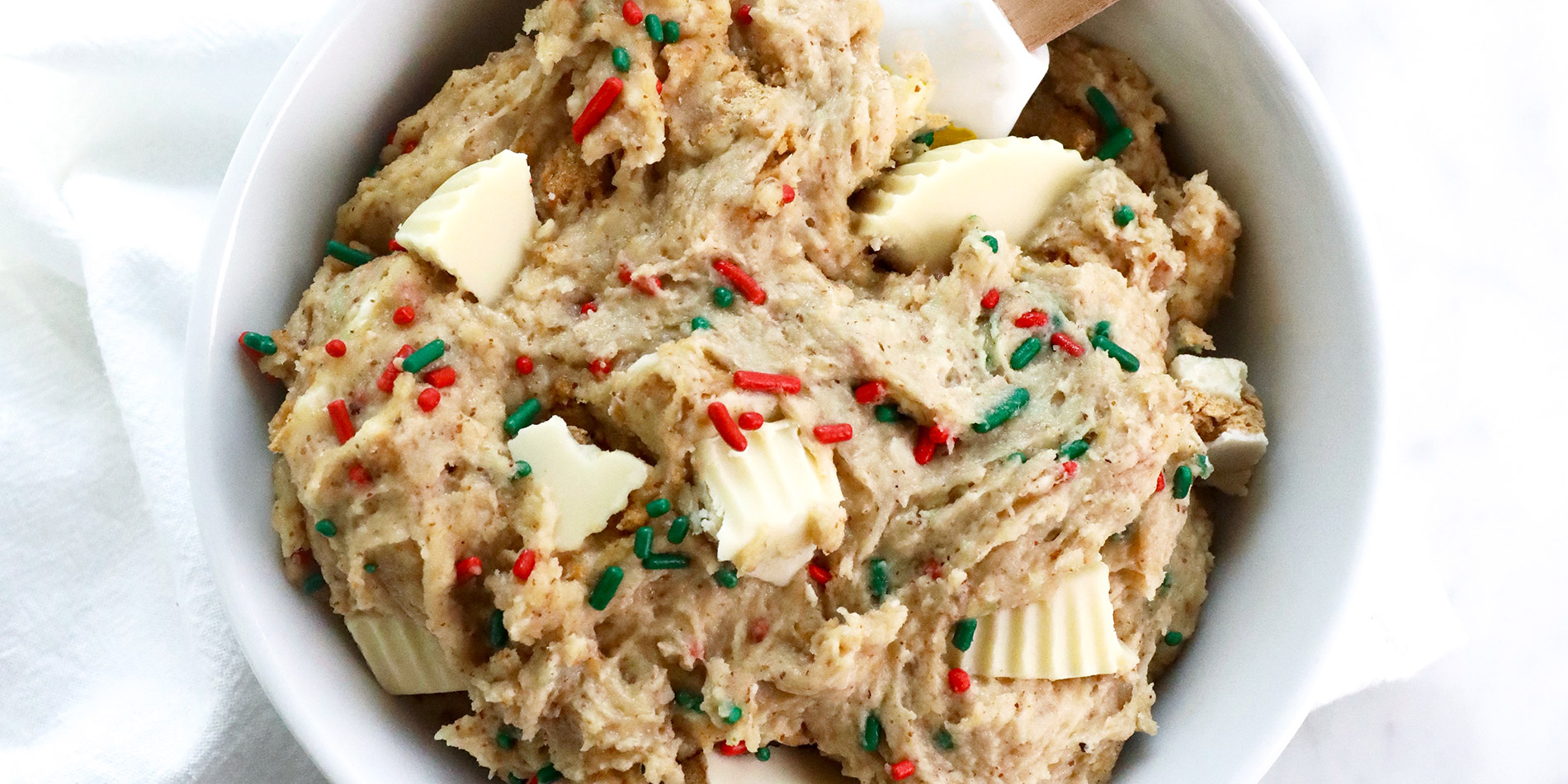 Edible White Chocolate Sugar Cookie Dough in a round white bowl with a wooden rubber spatula inside thumbnail image.