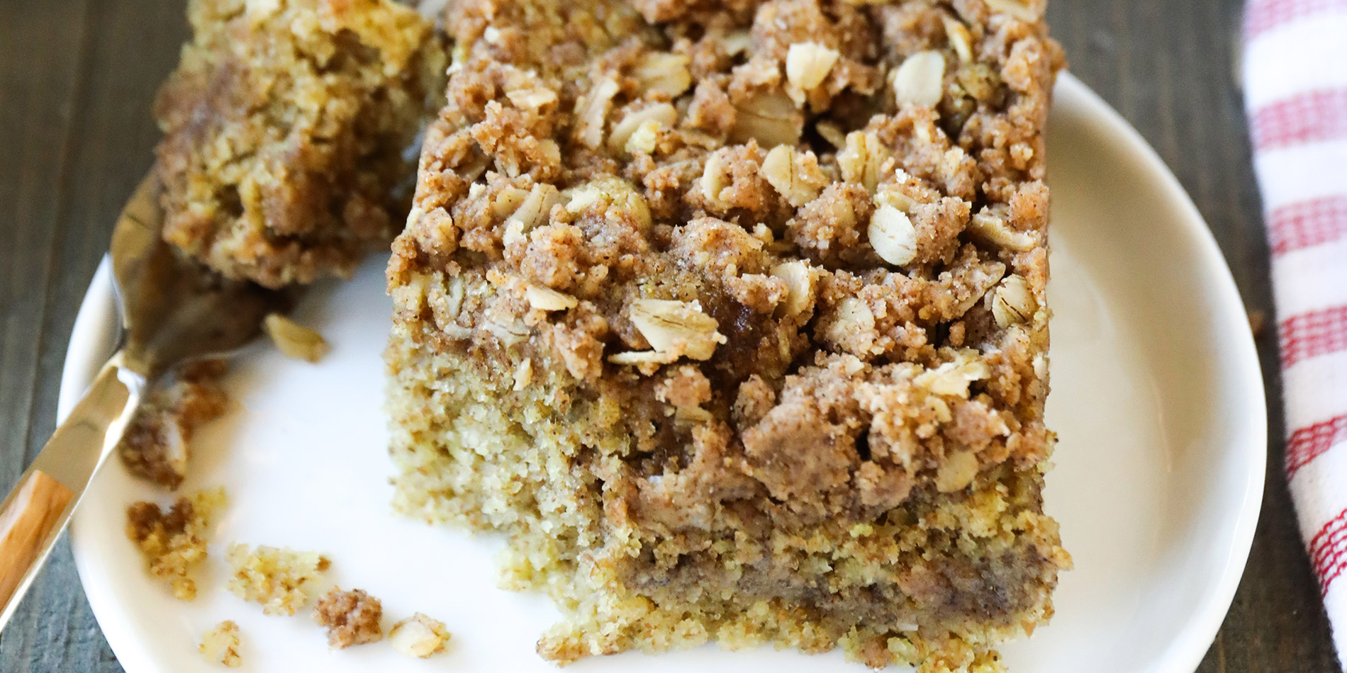 Maple Almond Butter Coffee Cake on a white plate with the corner cut with a fork on a wood background with tray and jar