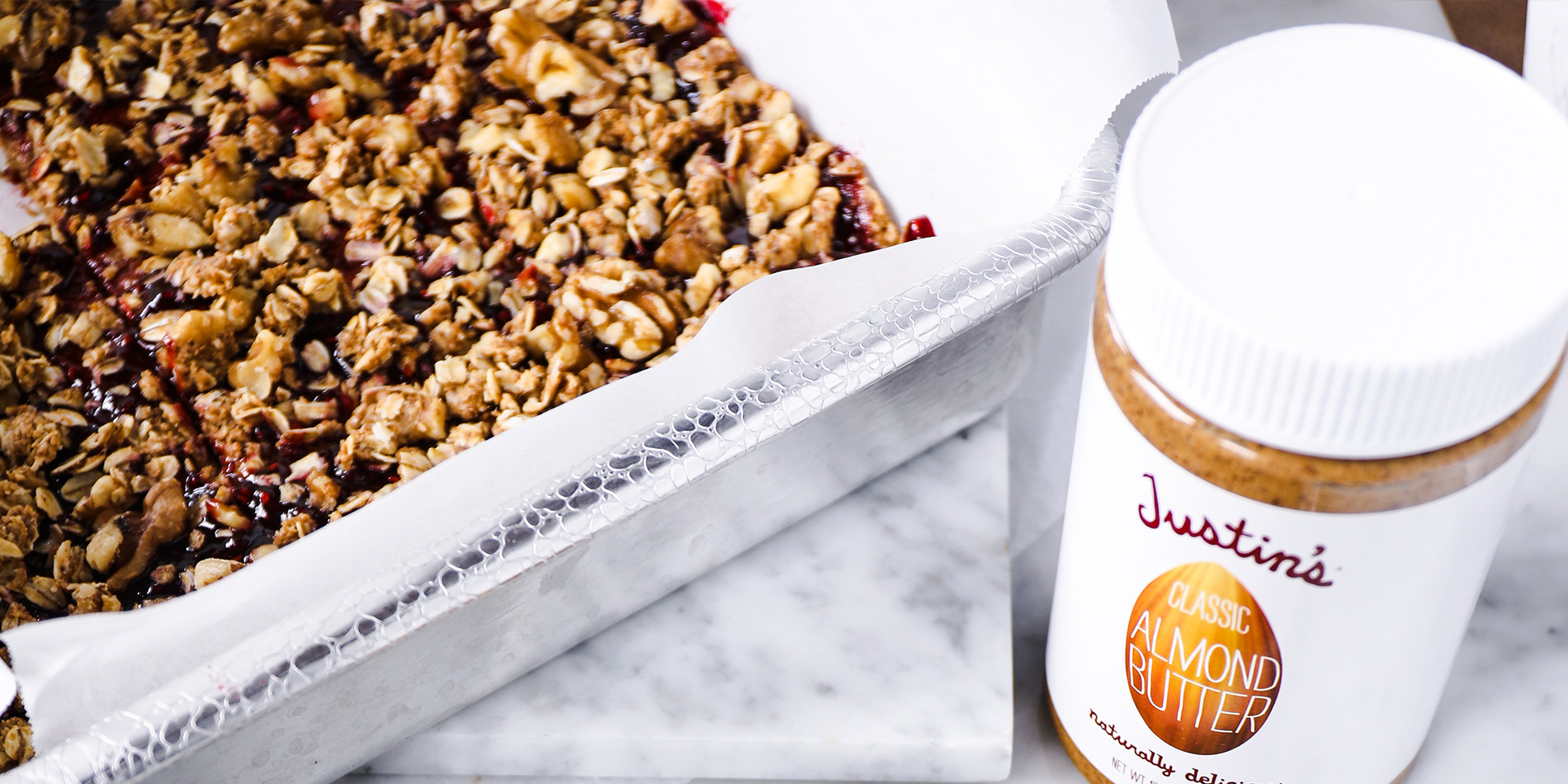 No-Bake Almond Butter and Jelly Breakfast Squares on a white tray with a jar of JUSTIN'S® Classic Almond Butter on the side thumbnail image.