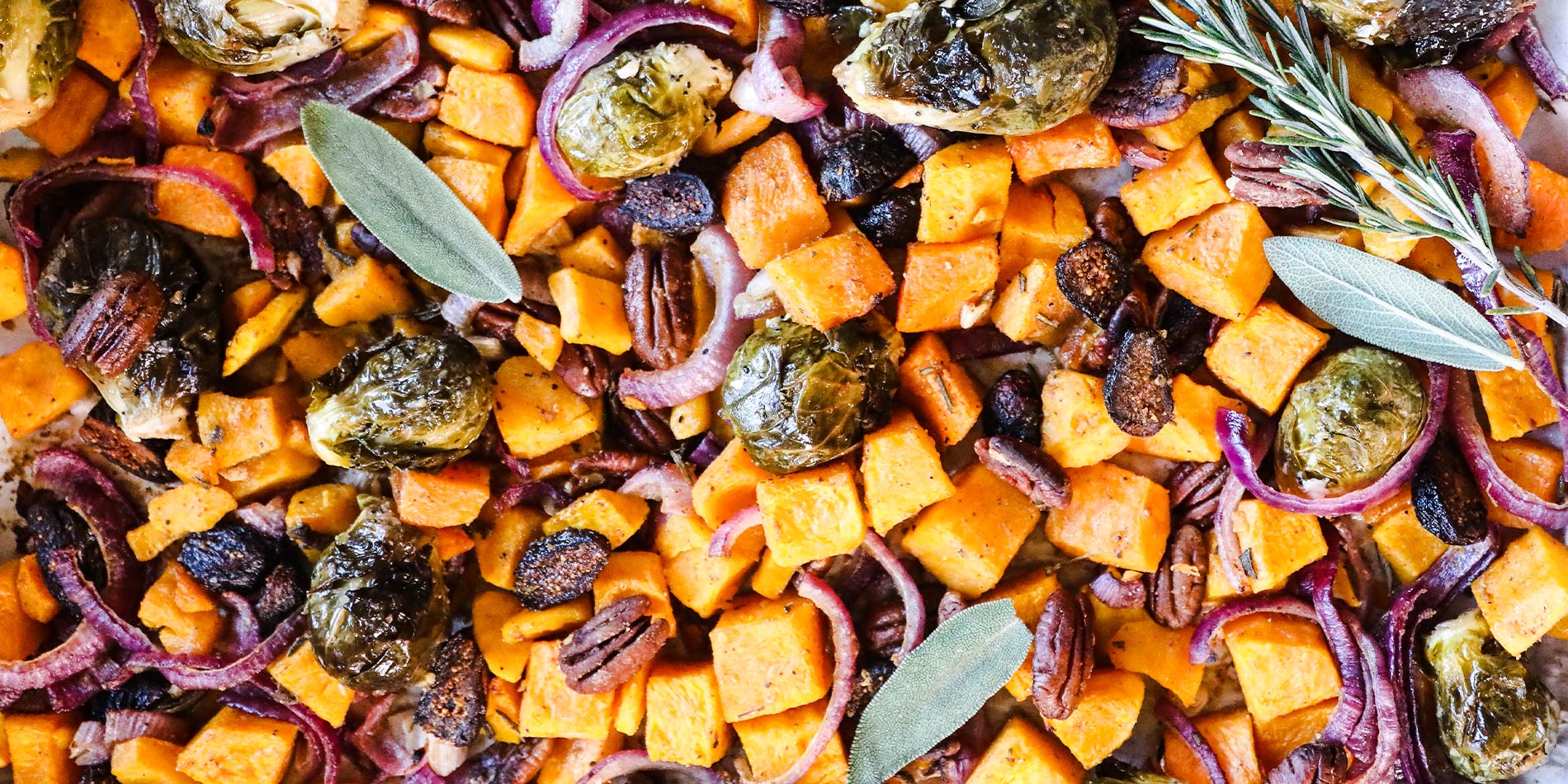 Nutty Butternut & Brussels Hash in a tray with parchment paper on a white background with golden fork and knife