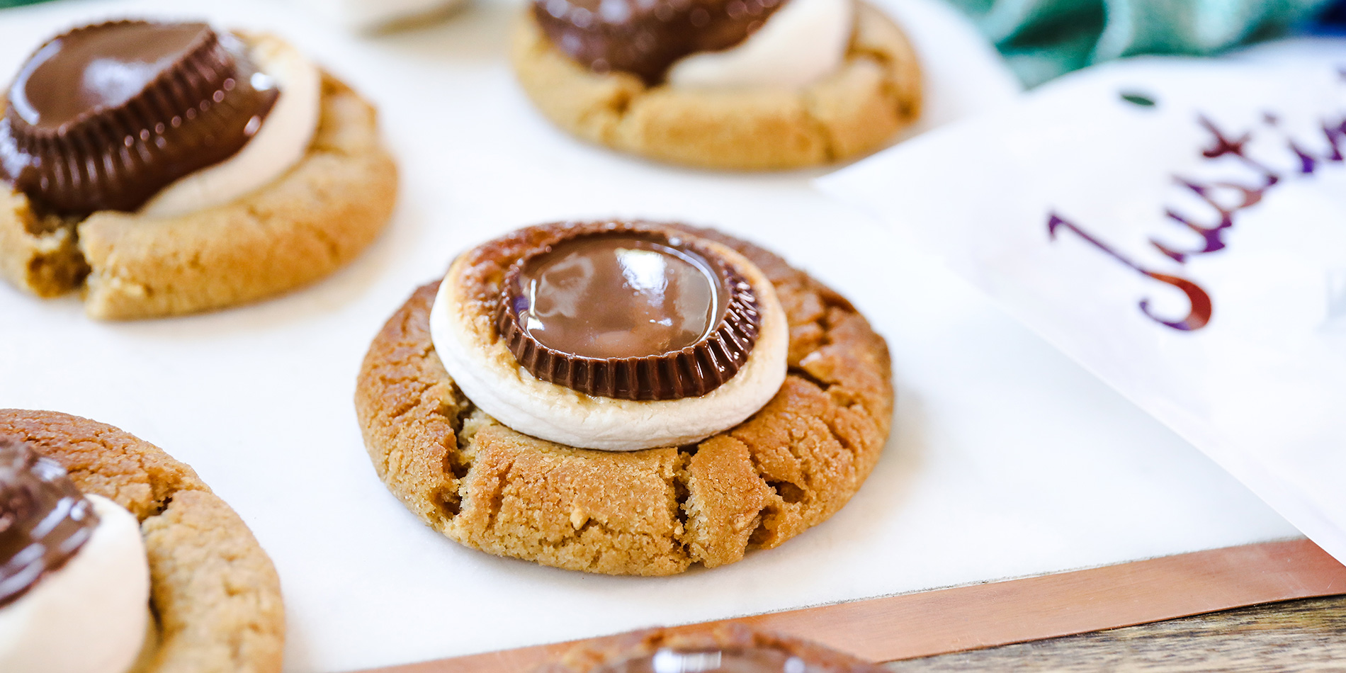 Peanut Butter Cup S'mores Cookies placed on white paper with marshmellows in the background with green cloth