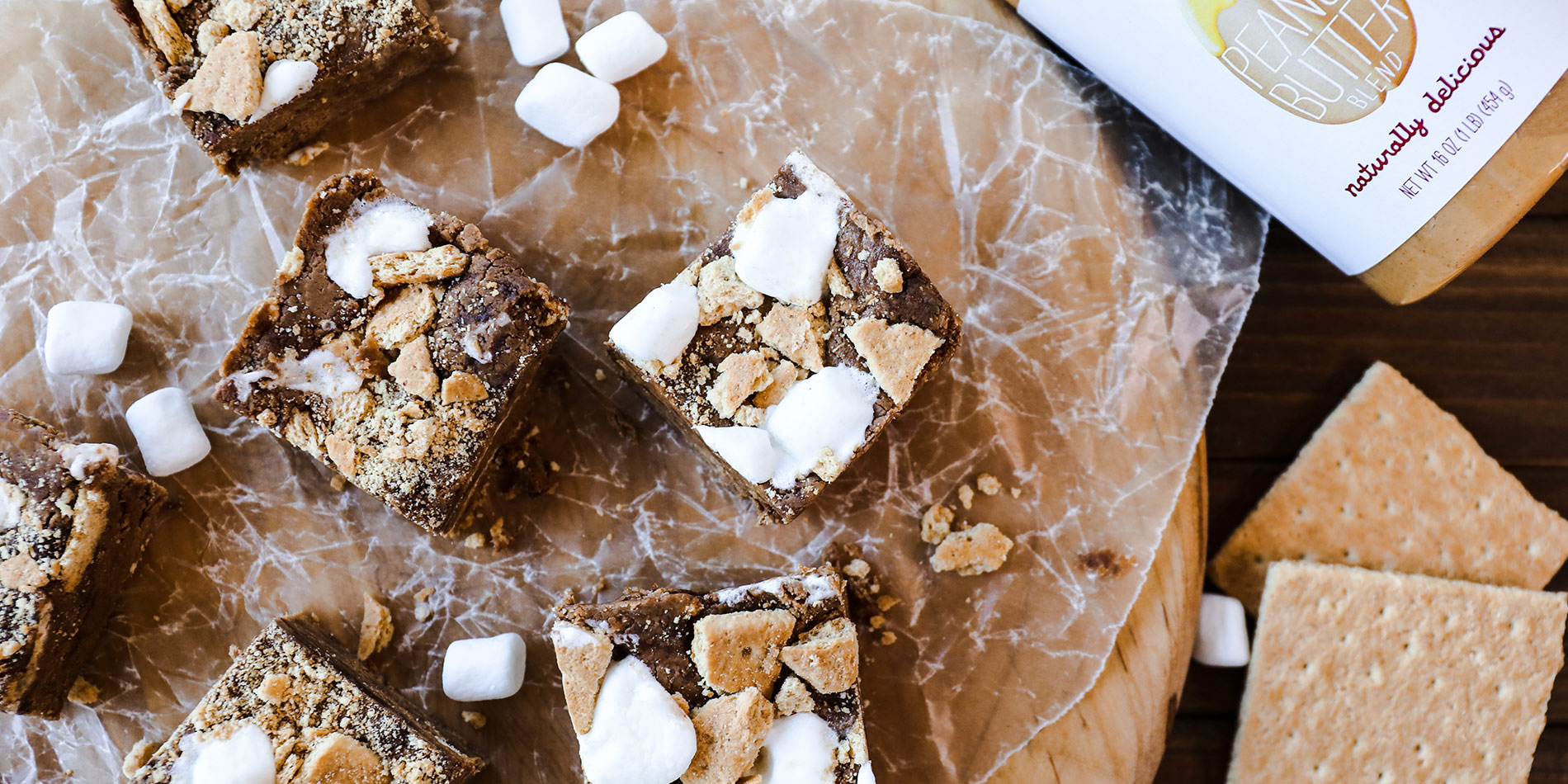 Peanut Butter S'mores Protein Fudge on square-cut crumpled clear parchment paper on a wood tray with a darker wood background