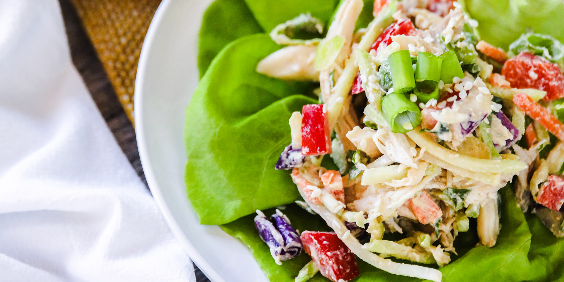 Thai Peanut Chicken Lettuce Wraps on a white round plate on a straw place mats beside a white cloth