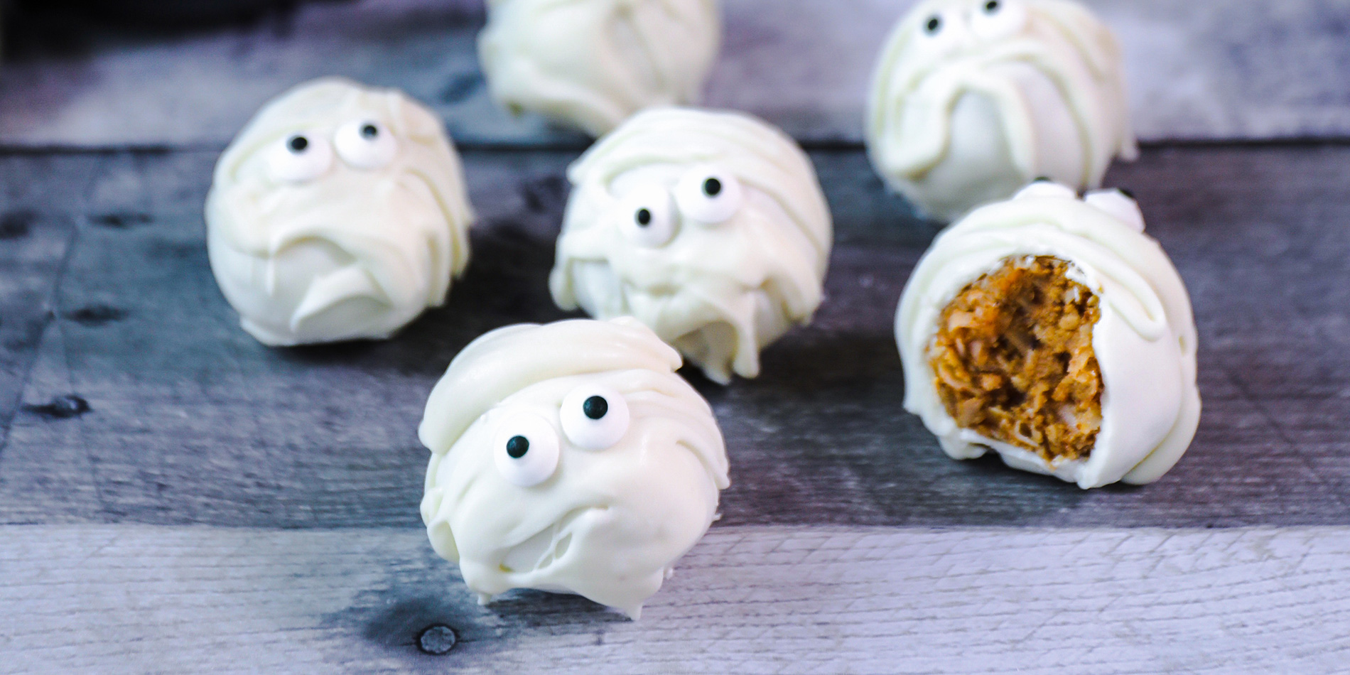 White Chocolate Almond Butter Mummies on a wood top with cutlery, straws, peanut butter jar in the background