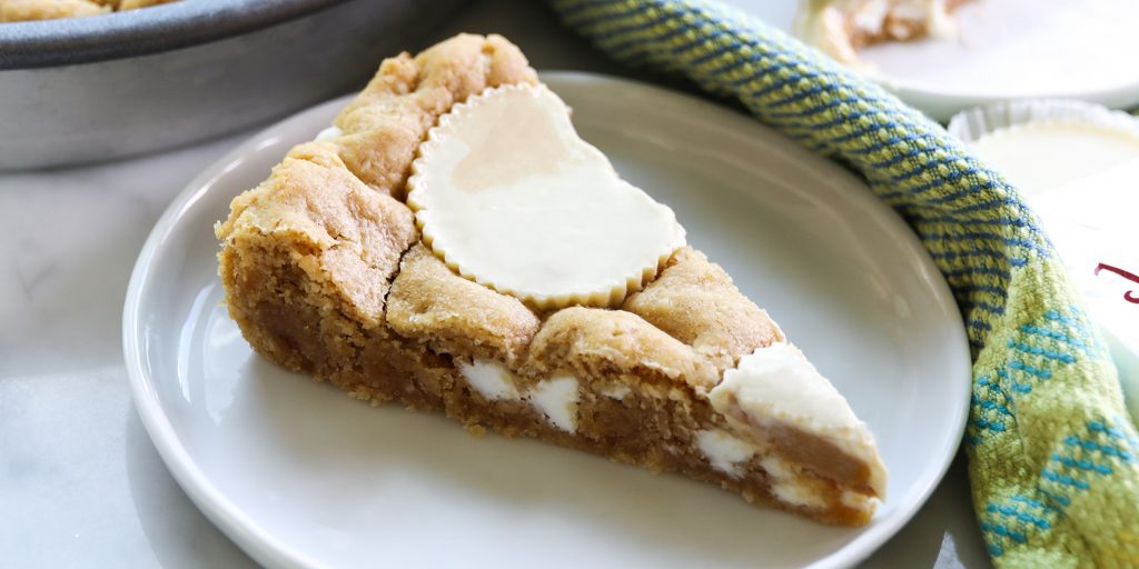 White Chocolate Peanut Butter Cup Cookie Cake on a white plate on a white background with green cloth