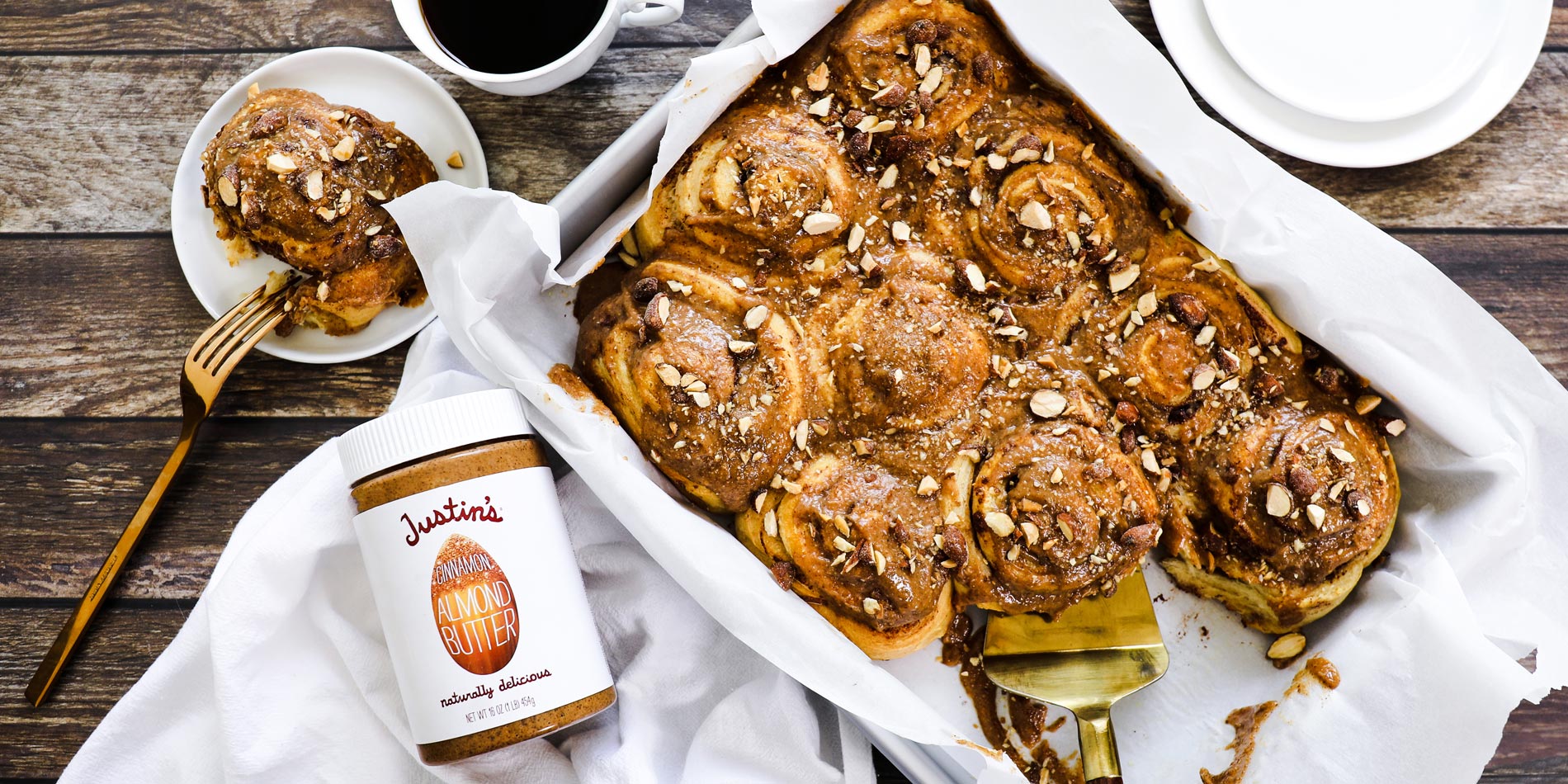 Almond Butter Cinnamon Rolls on a parchment sheet tray on a wooden background with a cup of coffee