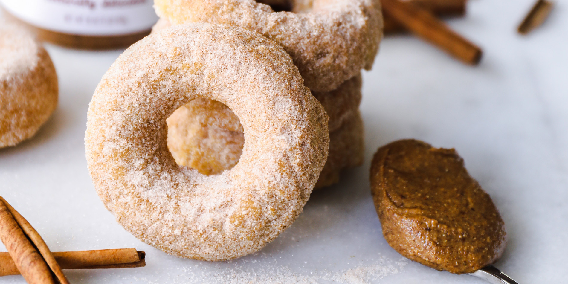 Baked Cinnamon Almond Butter Churro Doughnuts with cinnamon sticks in the background on a white background