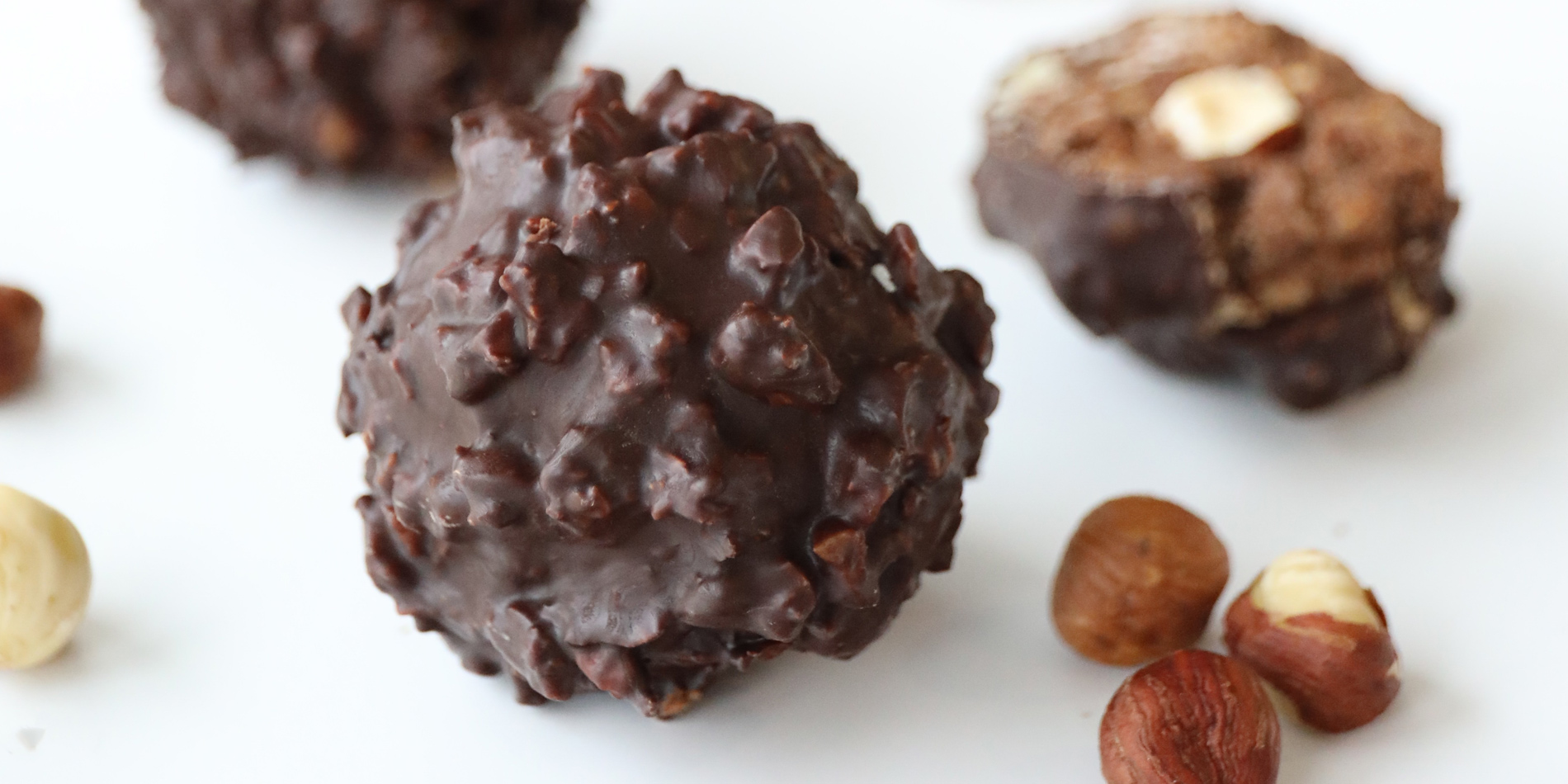 Chocolate Hazelnut Truffles on a white background with hazelnuts with blurred Justin's peanut butter jar