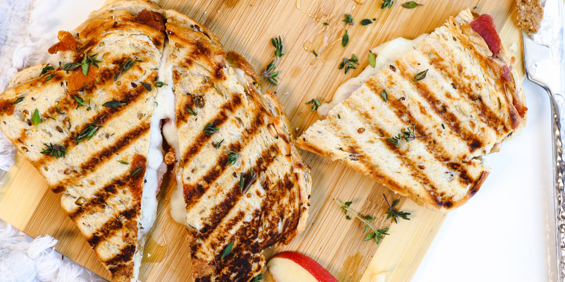 Cheesy Almond Butter Apple and Bacon Panini on a wooden cutting board with apple slices on a white background