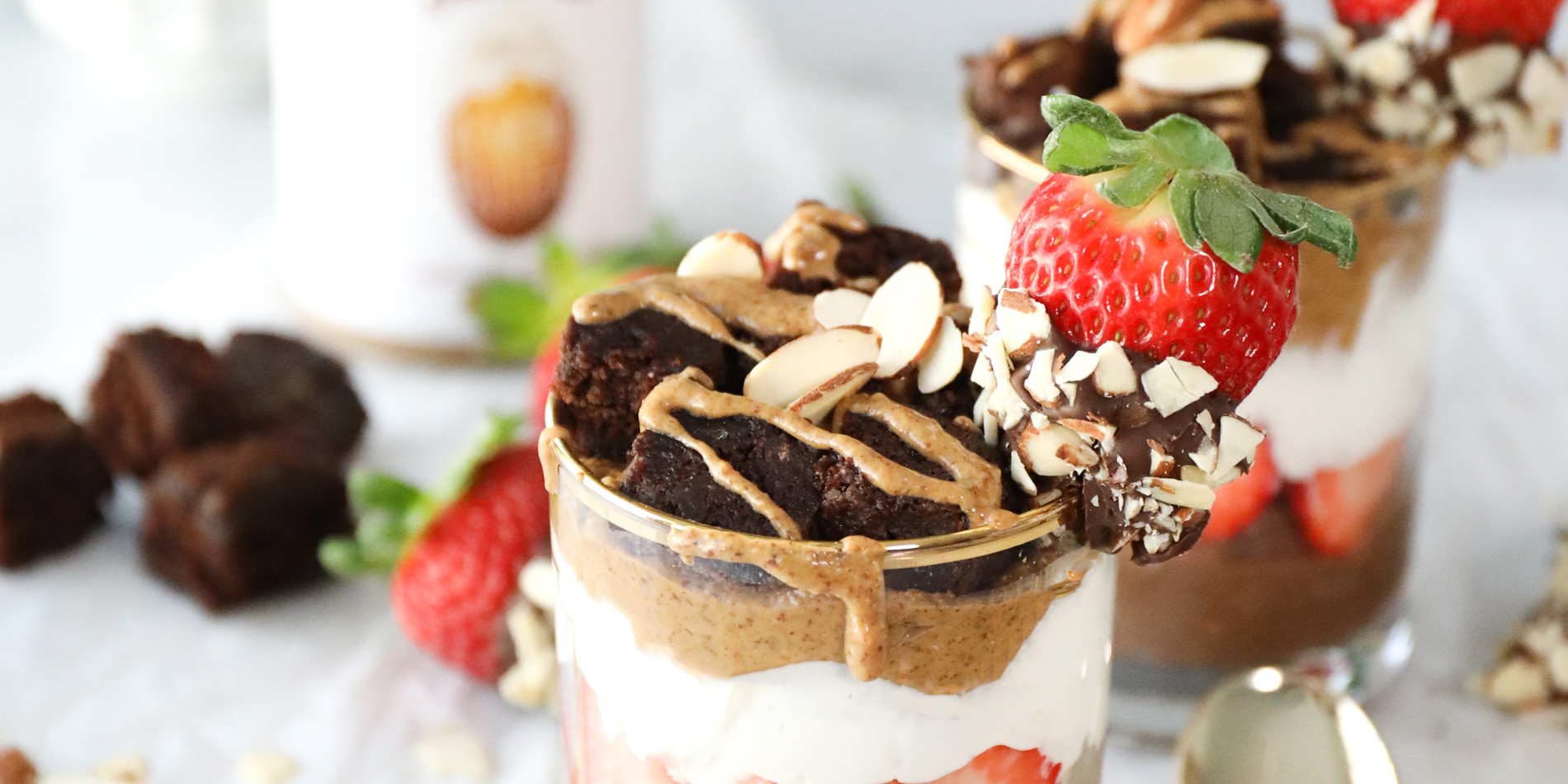 Chocolate Covered Strawberry and Almond Butter Parfait with gold spoons and chocolate fudge chunks in a white tabletop