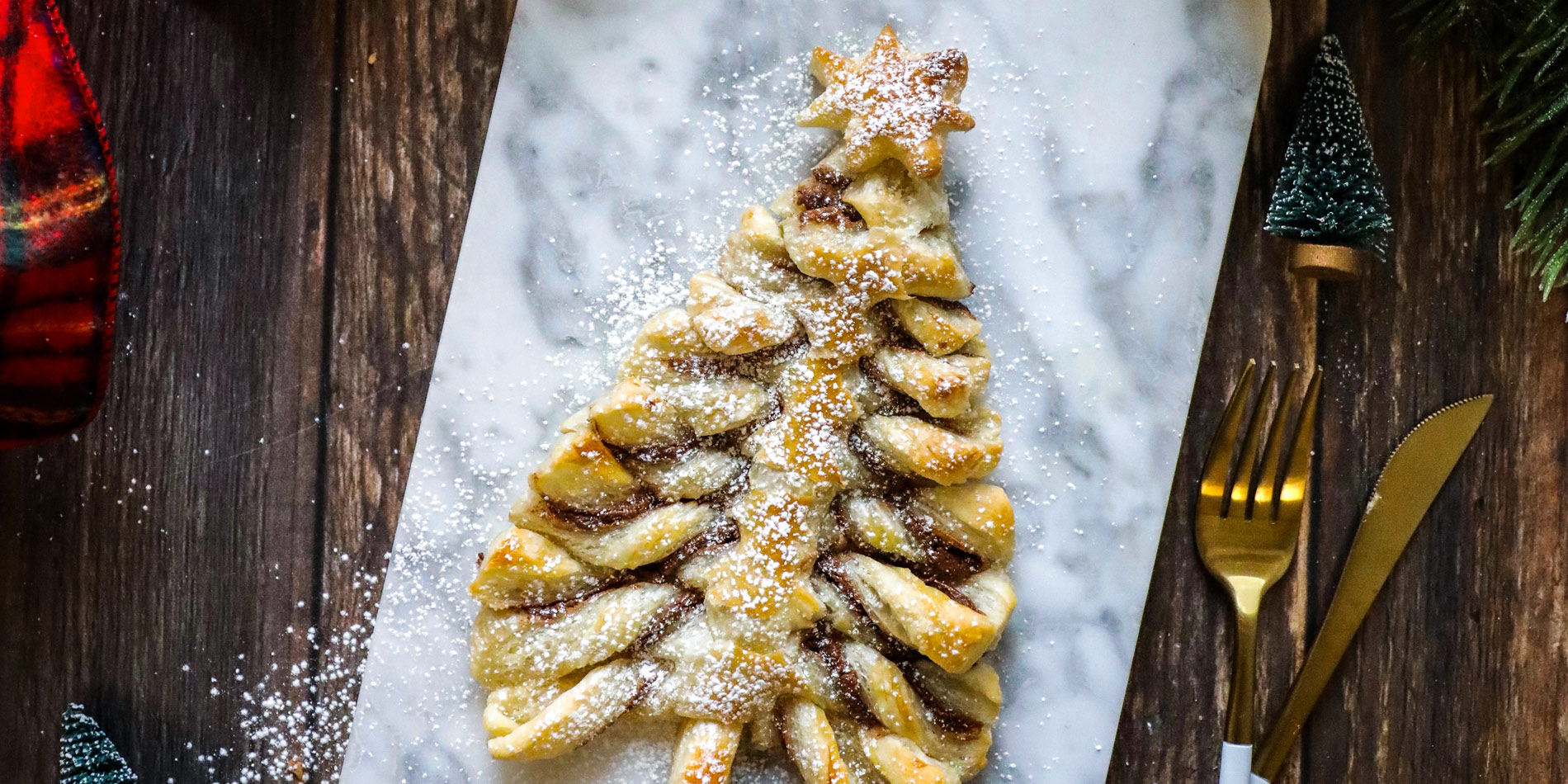 Chocolate Hazelnut PasTREE on a marble serving tray with golden cutlery, pine trees, Christmas ribbons on a wooden background