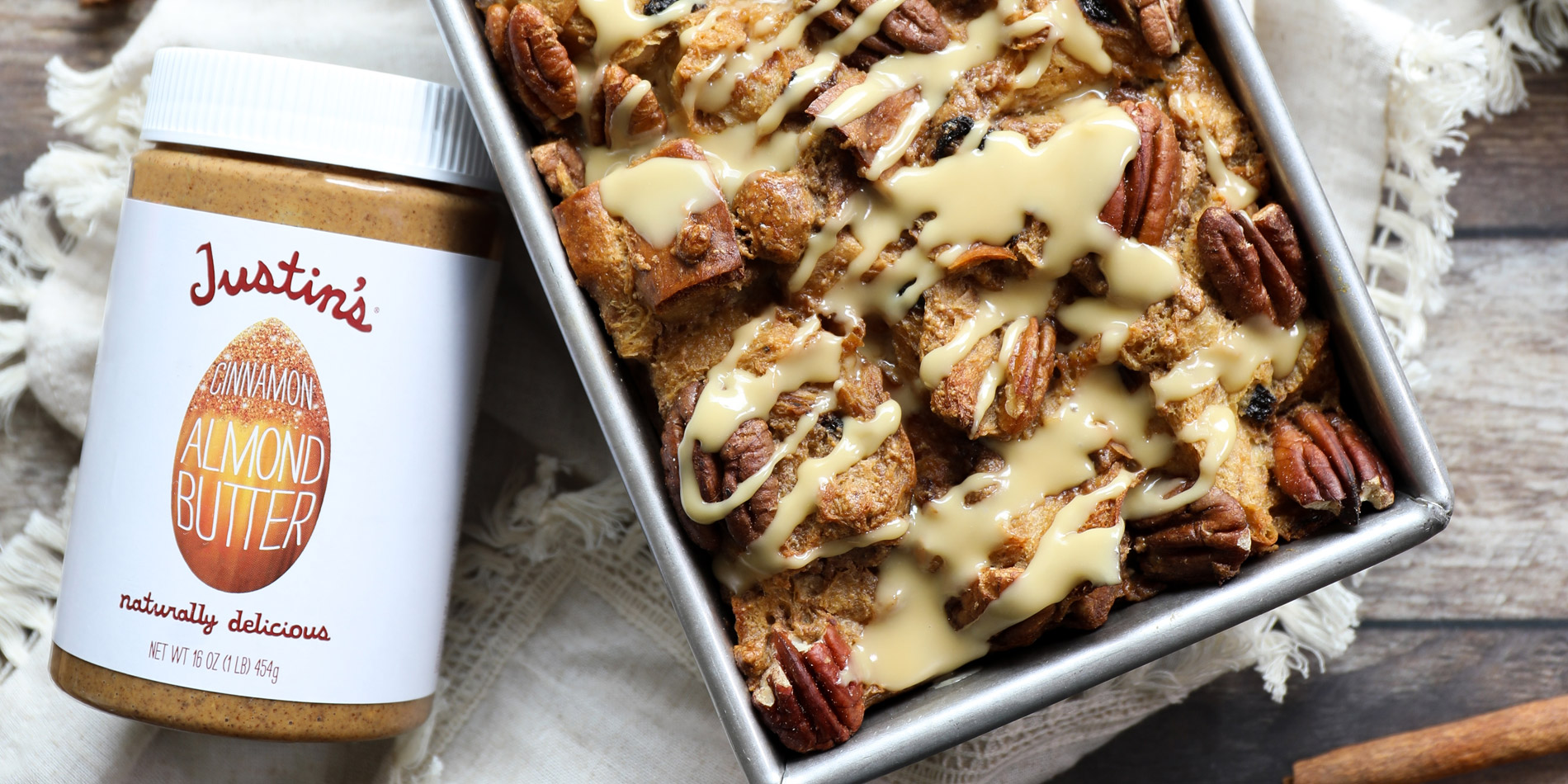 Cinnamon Almond Butter Bread Pudding Loaf in a tray with cinnamon sticks, oven mitts, and blue dishes in a wooden background
