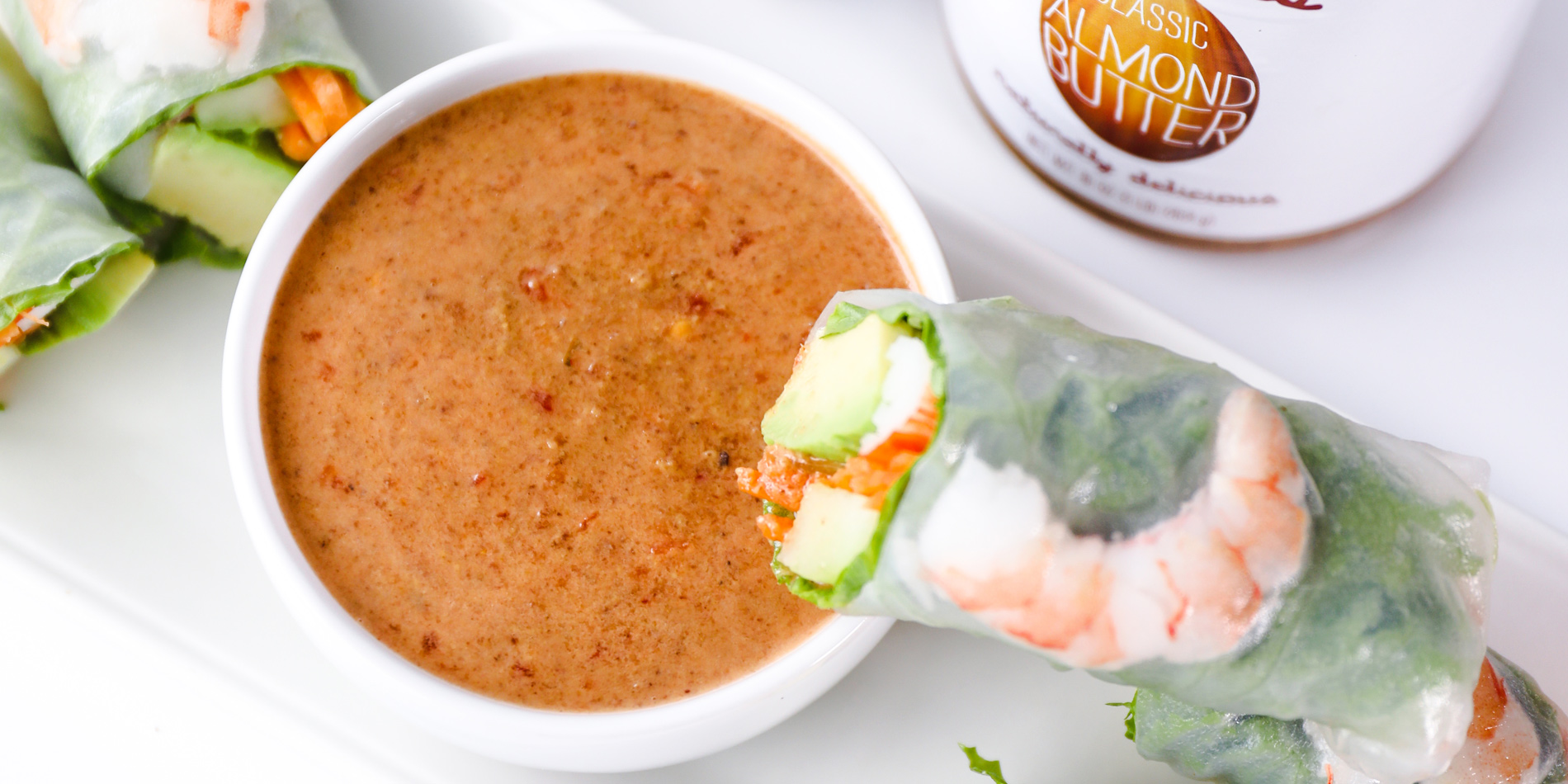 Ginger Almond Sauce with Vietnamese shrimp fresh rolls on white plate with ginger and peanut butter jar in white background