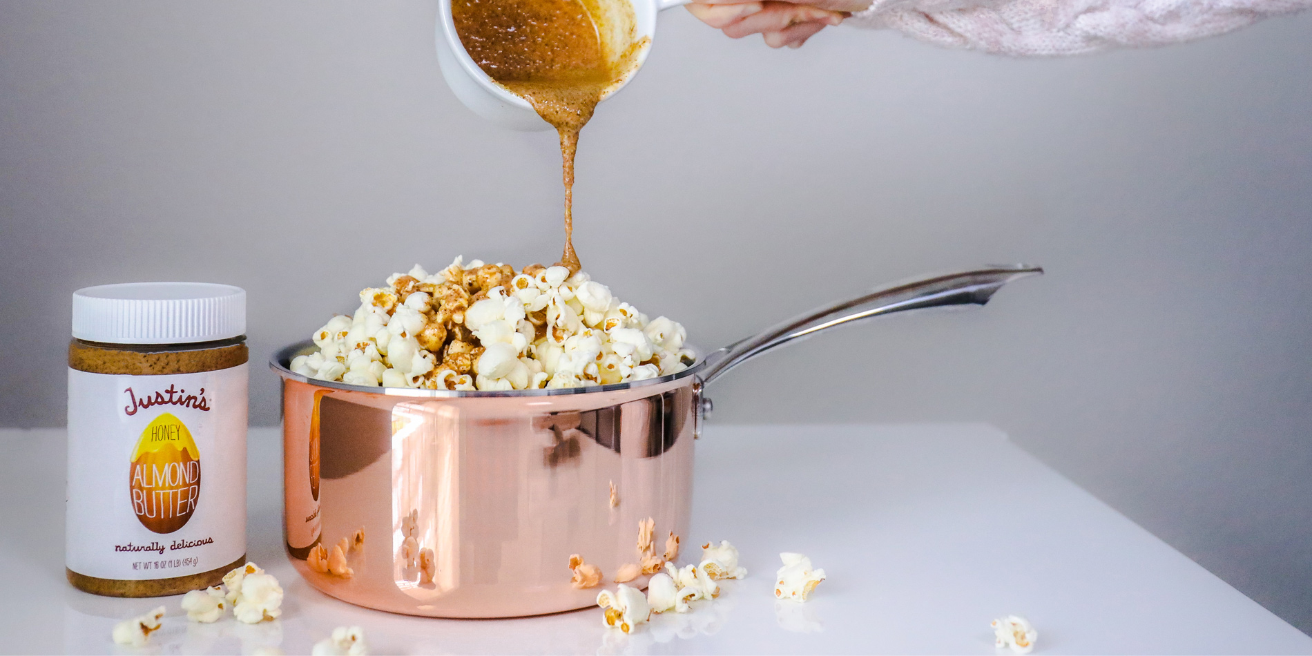 Honey Almond Buttered Popcorn in a pink pan with honey almond butter poured from top by a human hand on a white background