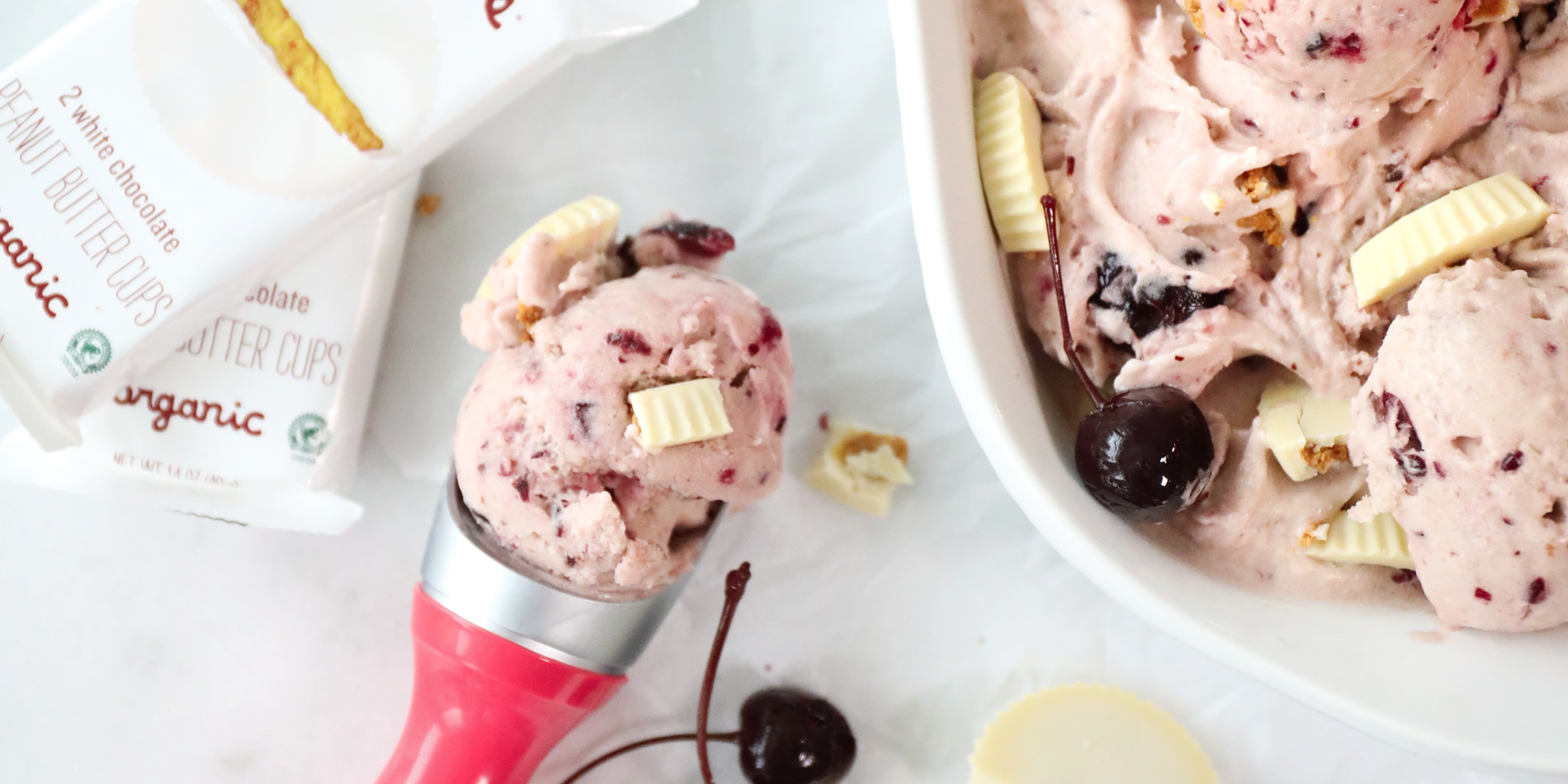 Nutty White Chocolate Cherry “Nice” Cream scooped out from white tray with scattered cherries and Justin's peanut butter cups