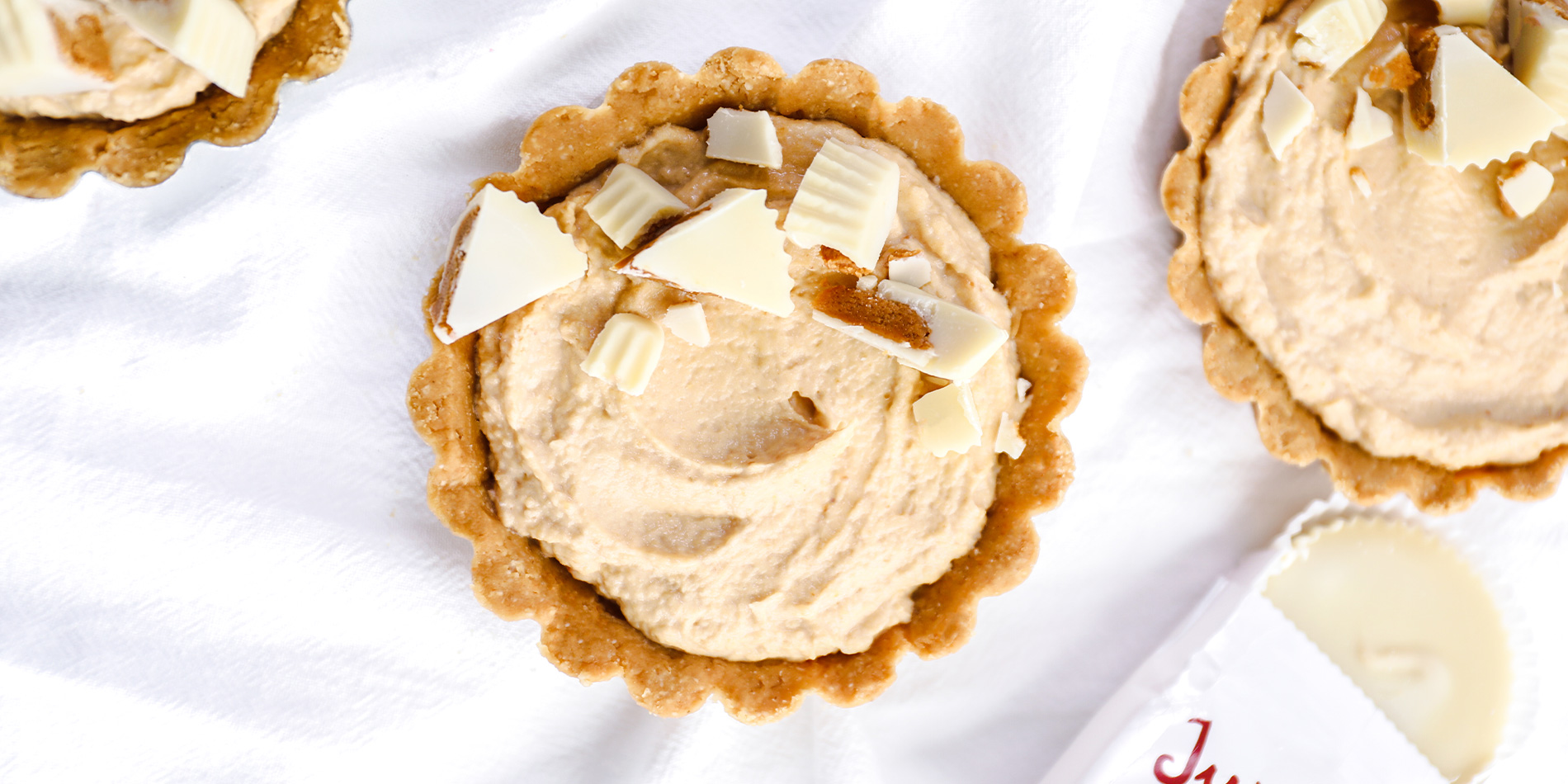 No Bake White Chocolate Peanut Butter Cheesecakes on a white cloth background with Justin's white chocolate peanut butter cup