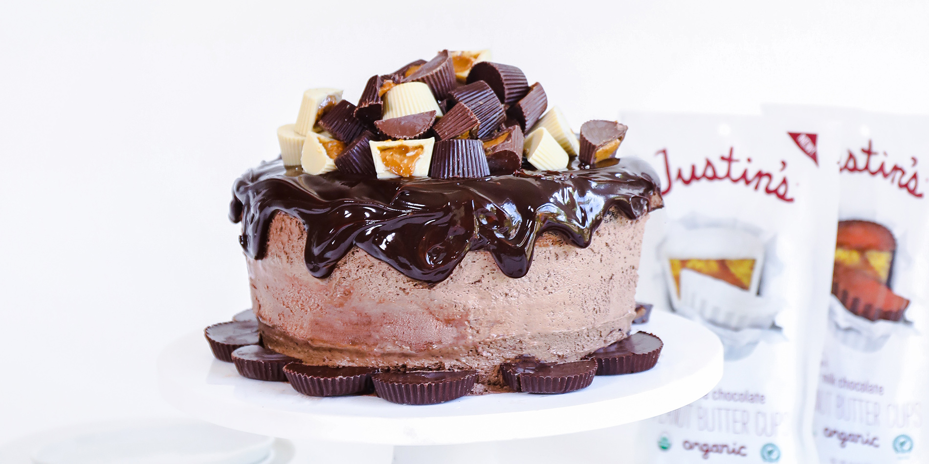 Peanut Butter Cup Ice Cream Cake on a white cake tray with a slice on a white plate with Justin's products in background