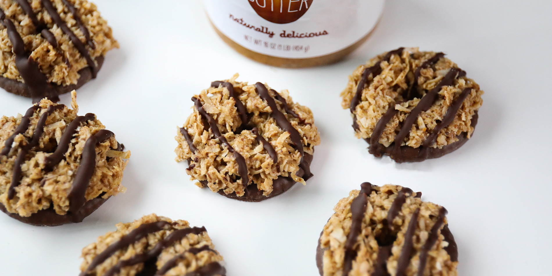 Sweet & Salty Almond Butter Coconut Delights scattered in a white background with Justin's peanut butter jar