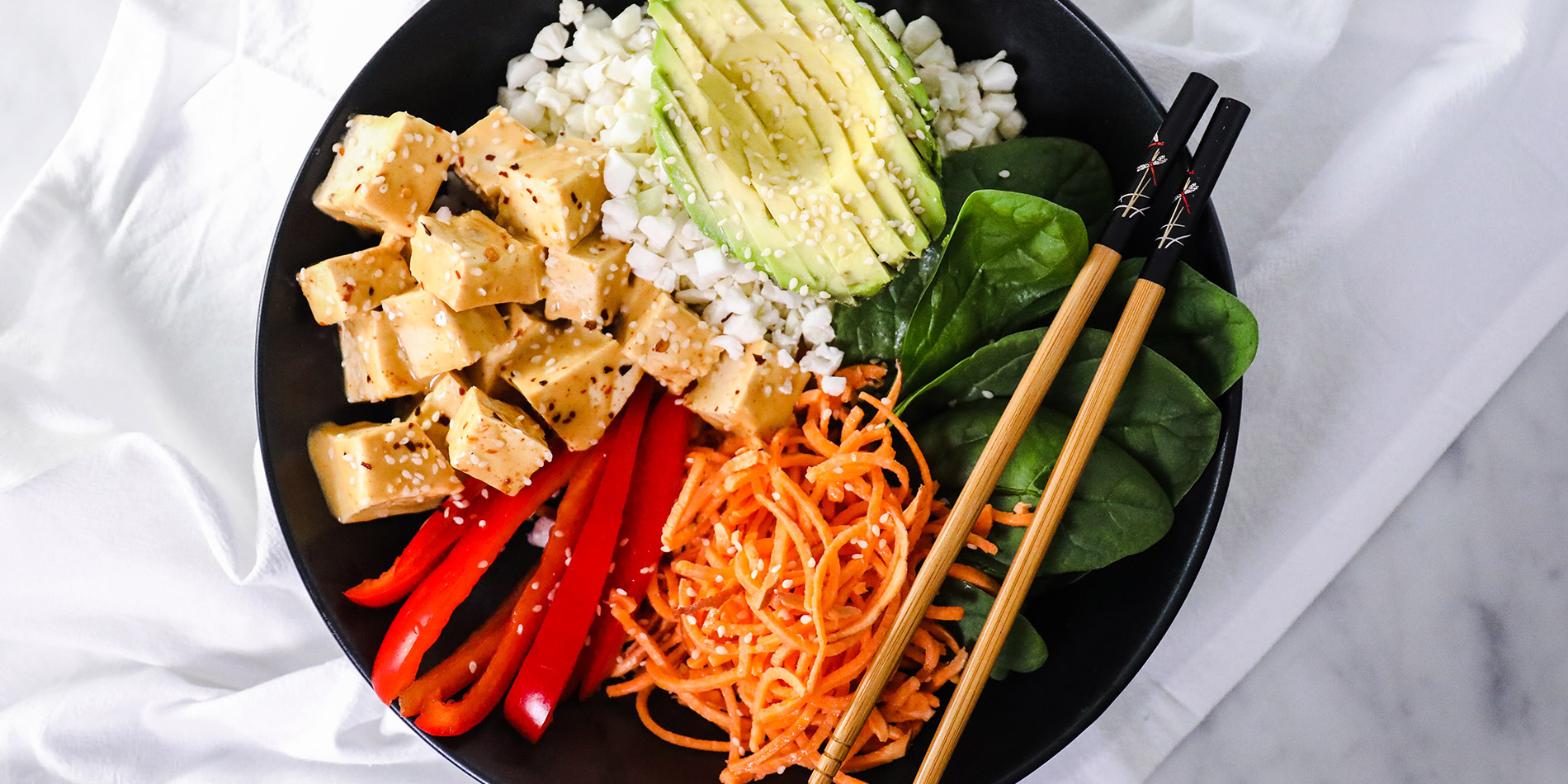 Thai Peanut Tofu Bowl in a black bowl with chopsticks from the top view on a white background with a white cloth