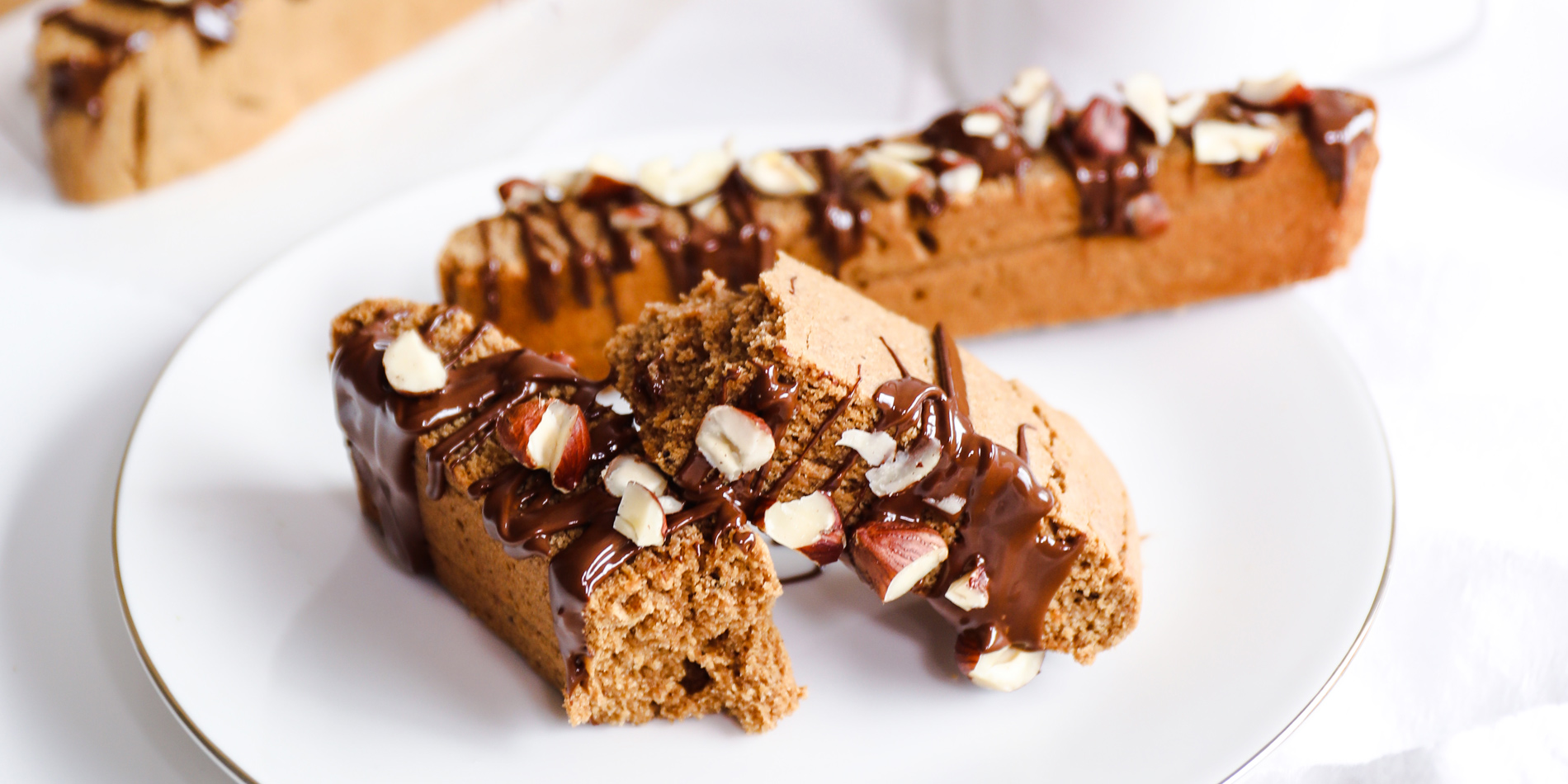 Chocolate Hazelnut Espresso Biscotti on a white plate with silver lining beside a cup of coffee in a white background