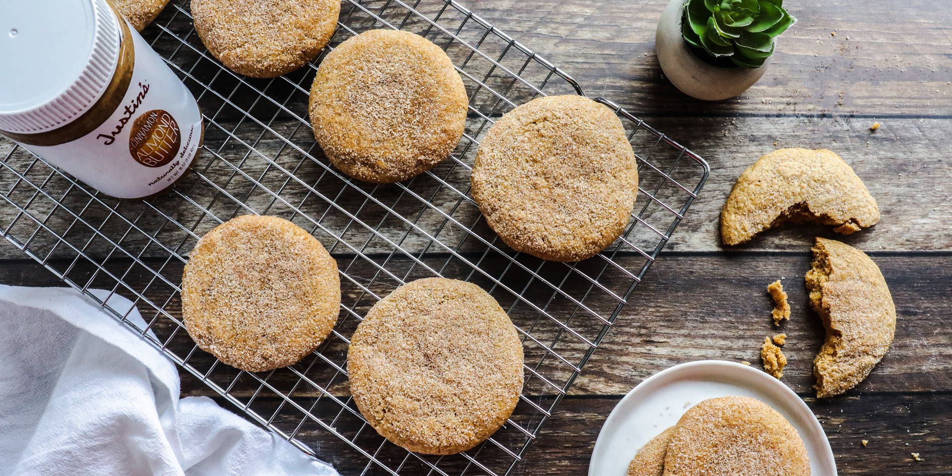 Cinnamon Almond Butter Snickerdoodles on a cooling rack with Justin's peanut butter jar and white cloth on a wood background