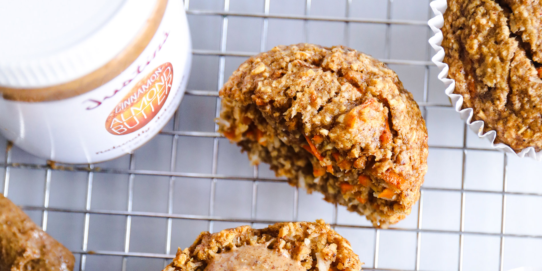 Cinnamon Almond Carrot Cake Muffins on a cooling rack with peanut butter spread on the half cut muffin on a white background