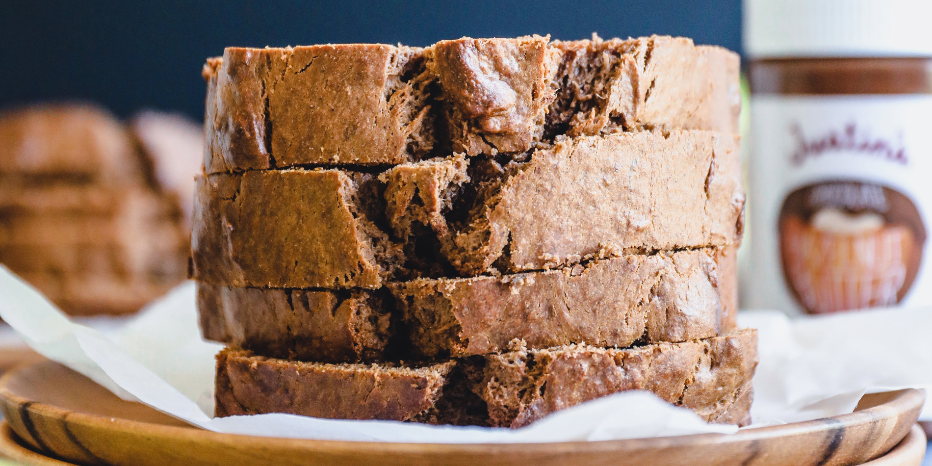 Dairy Free Chocolate Hazelnut Banana Bread stacked on parchment on two wooden dishes with whole banana on blue background